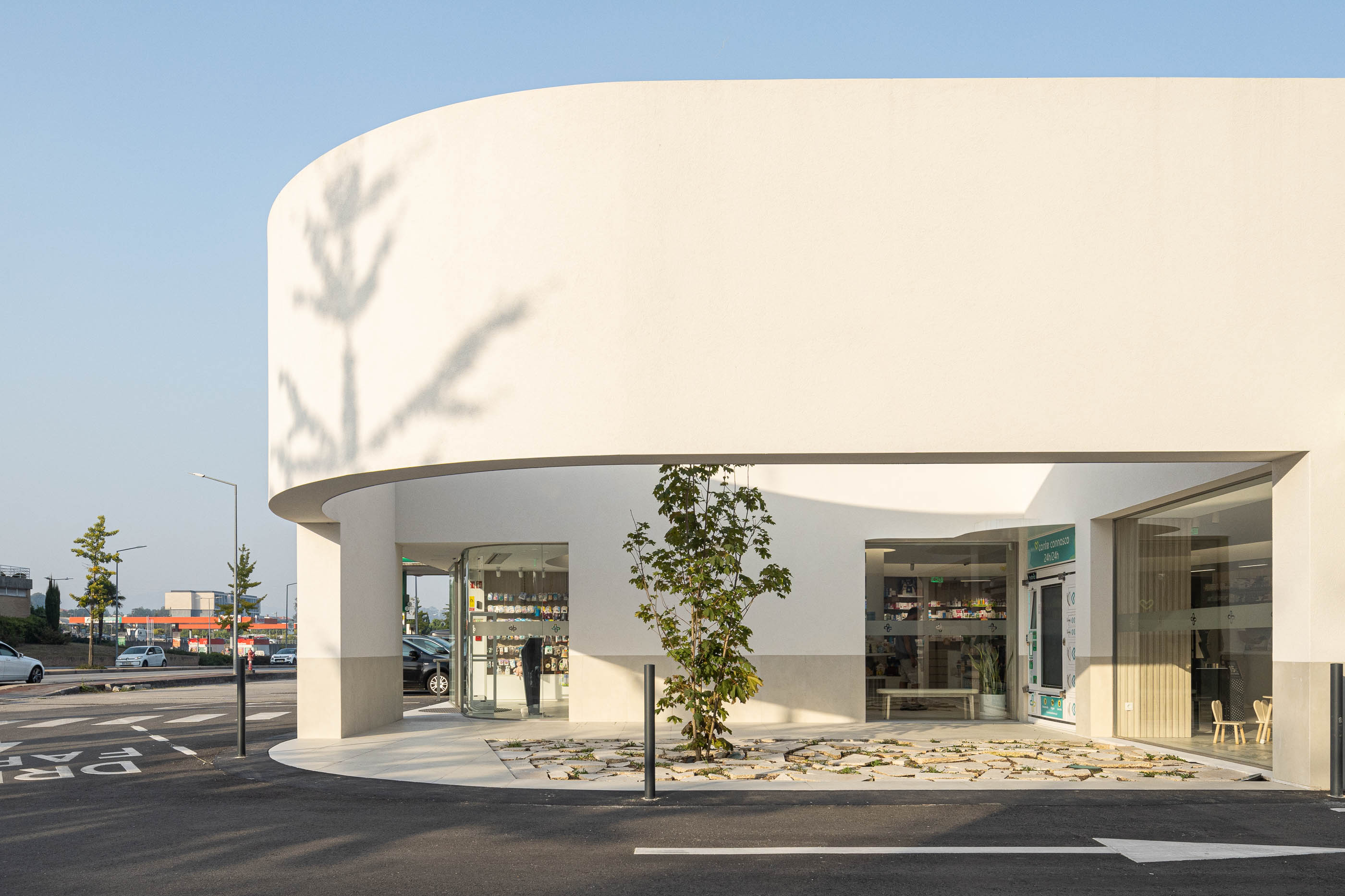 Exterior: Detalhe da porta de vidro curva e pavimento exterior em pedra. — Farmácia da Devesa arquitetura Tsou Arquitectos em Vila Nova de Famalicão