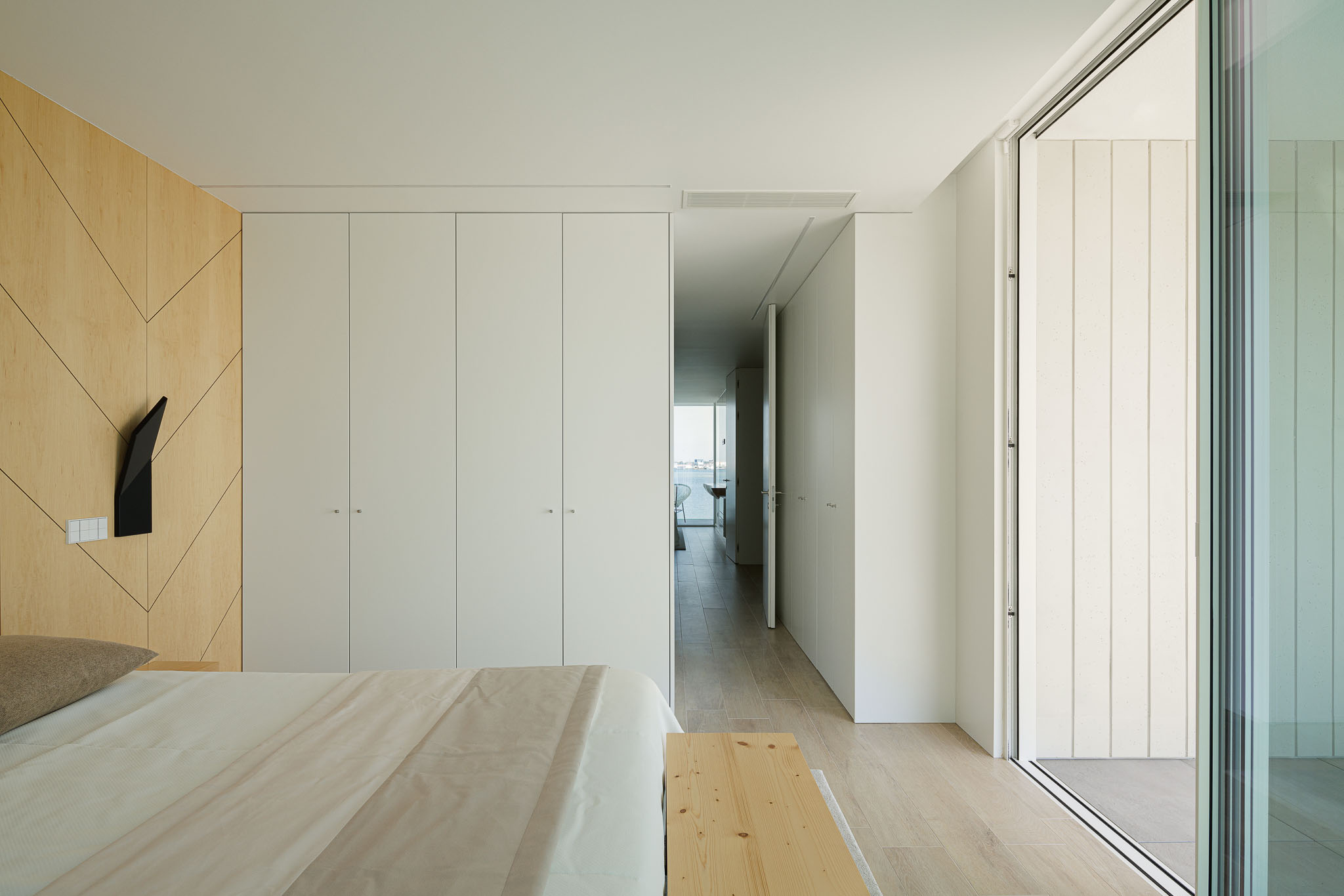 Quarto: Roupeiro branco embutido, pavimento em madeira clara e acesso à varanda com vista para a ria. — Moradia JD2 arquitetura Rui Rosmaninho Arquiteto em Ílhavo