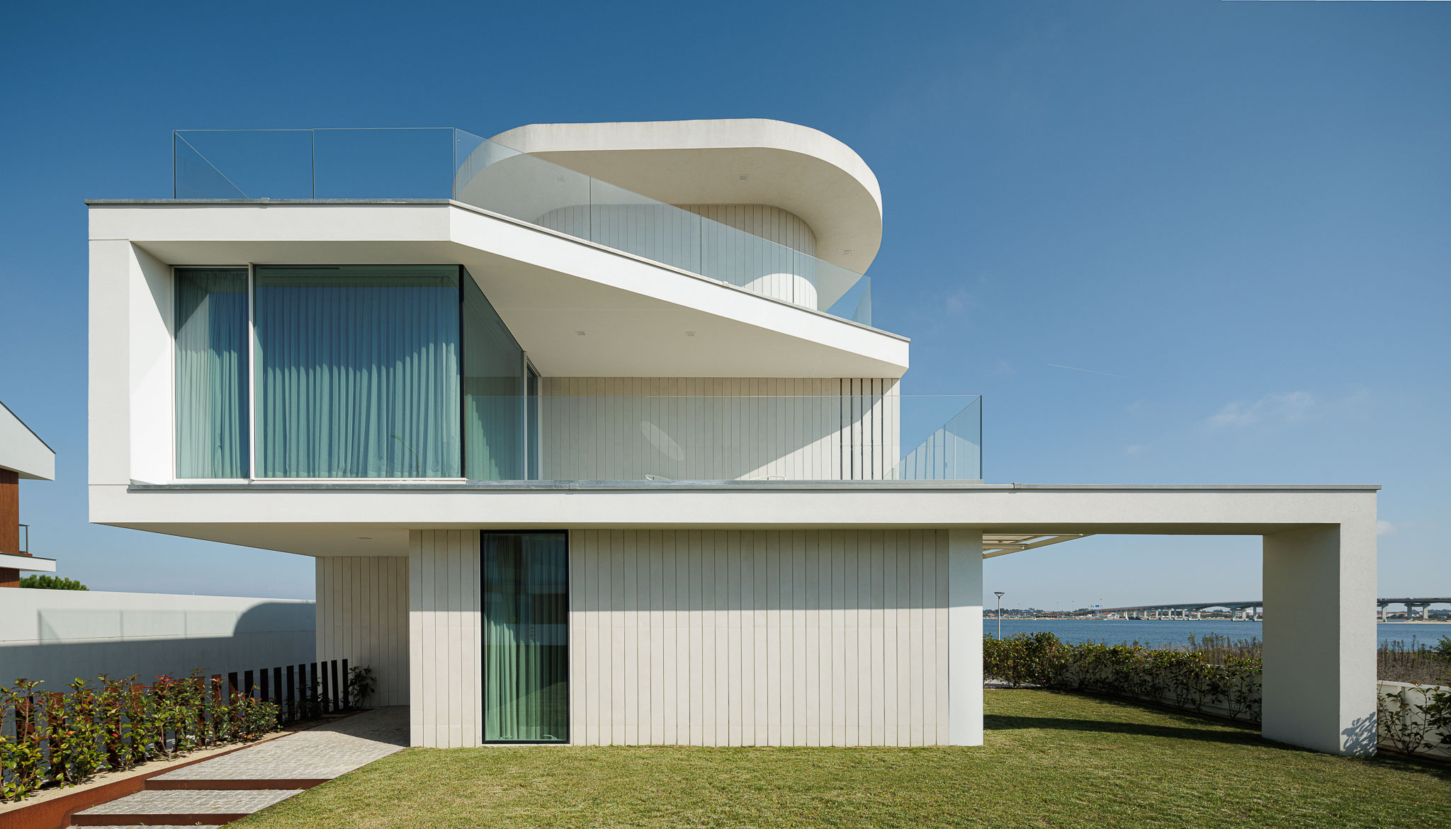 Exterior: Moradia moderna de três pisos com fachada branca, varandas com guarda em vidro e jardim relvado. — Moradia JD2 arquitetura Rui Rosmaninho Arquiteto em Ílhavo
