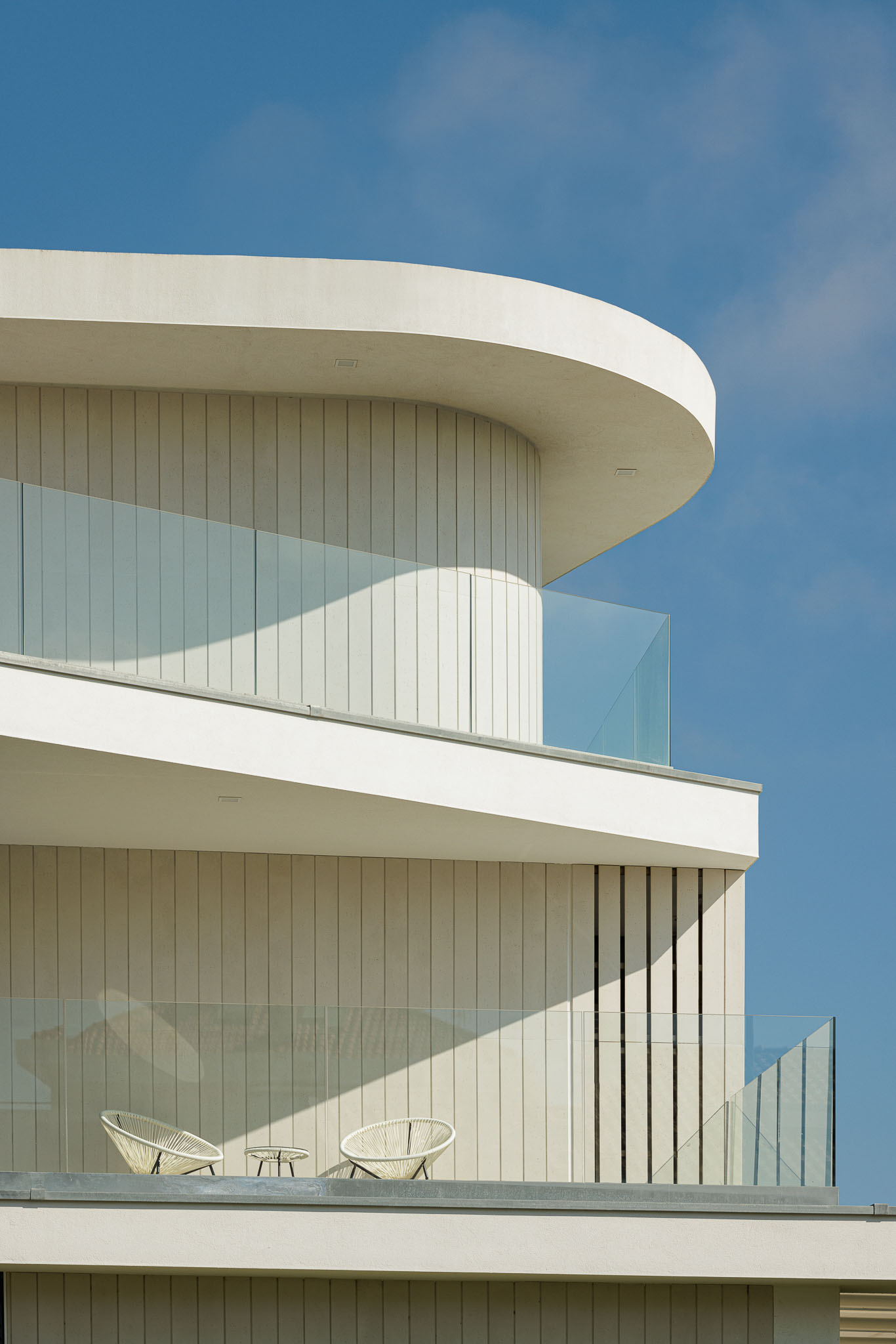 Exterior: Detalhe da fachada com elementos curvos, varandas com guarda em vidro e revestimento vertical branco. — Moradia JD2 arquitetura Rui Rosmaninho Arquiteto em Ílhavo