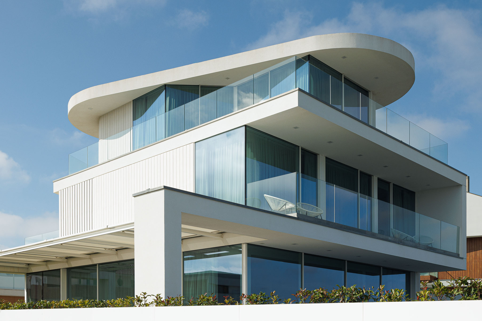 Exterior: Detalhe da fachada com elementos curvos, varandas com guarda em vidro e grandes janelas. — Moradia JD2 arquitetura Rui Rosmaninho Arquiteto em Ílhavo