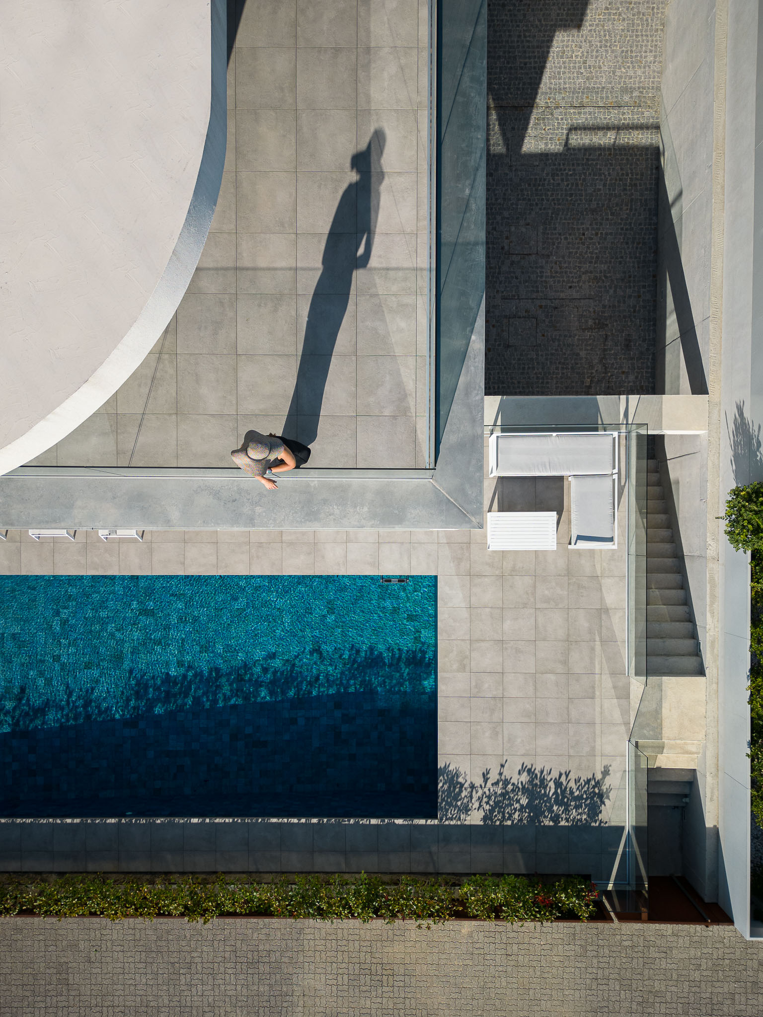Exterior: Vista aérea da piscina, pavimento cerâmico cinzento e área de lazer com espreguiçadeiras. — Moradia JD2 arquitetura Rui Rosmaninho Arquiteto em Ílhavo