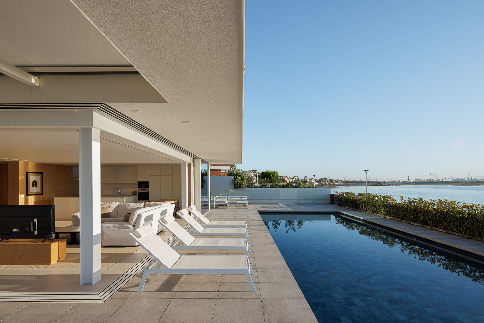 Exterior: Piscina com espreguiçadeiras brancas, pavimento cerâmico cinzento e vista para a ria. — Moradia JD2 arquitetura Rui Rosmaninho Arquiteto em Ílhavo