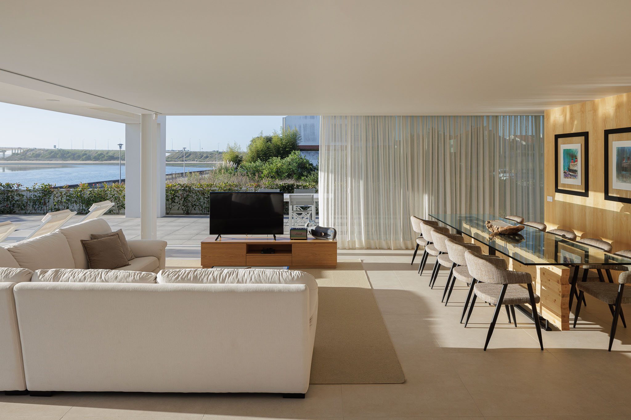 Sala de jantar: Mesa de jantar com tampo de vidro e cadeiras cinzentas, parede revestida a madeira clara. — Moradia JD2 arquitetura Rui Rosmaninho Arquiteto em Ílhavo