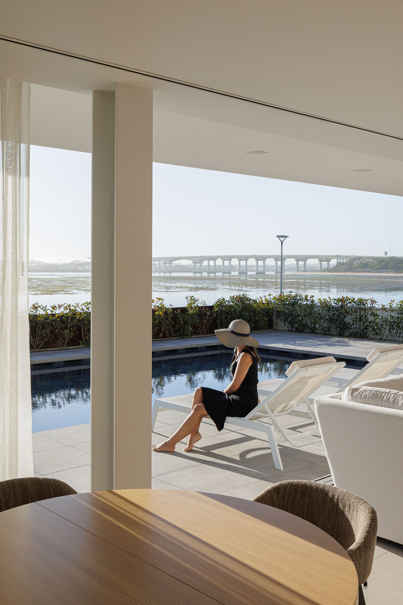 Exterior: Pessoa de costas junto à piscina, com vista para a ria e ponte. — Moradia JD2 arquitetura Rui Rosmaninho Arquiteto em Ílhavo