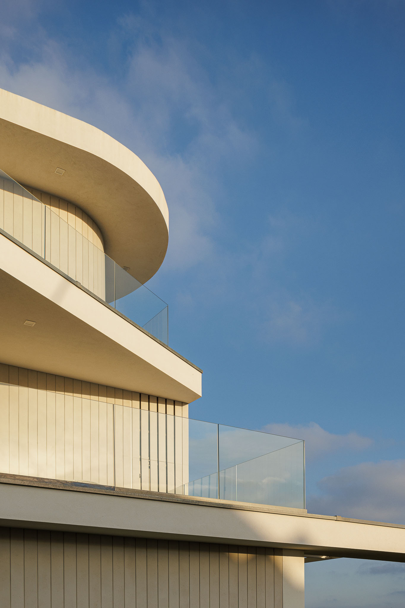 Exterior: Moradia moderna com fachada branca, varandas com guarda em vidro e cobertura curva. — Moradia JD2 arquitetura Rui Rosmaninho Arquiteto em Ílhavo