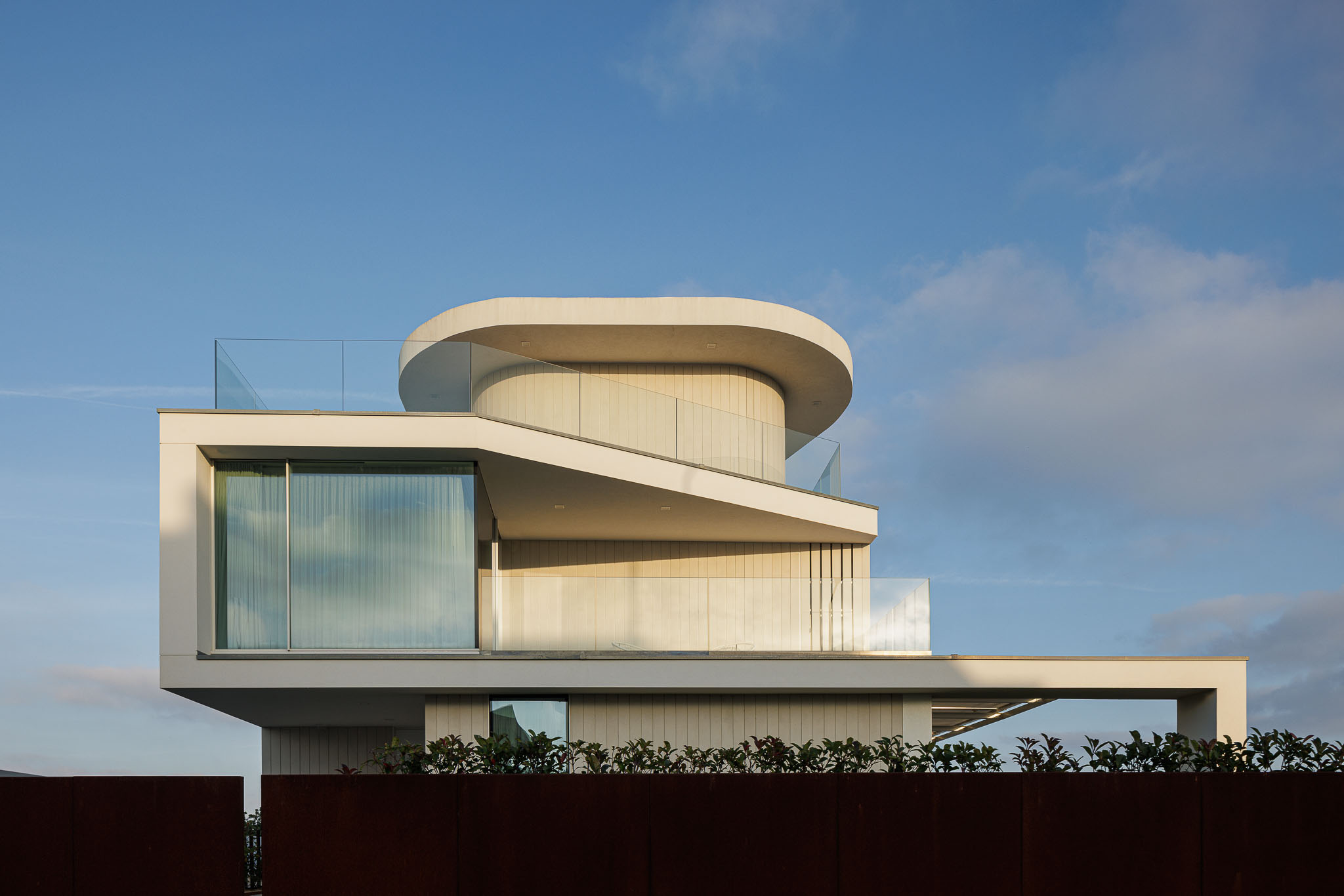 Exterior: Detalhe da fachada com elementos curvos, varandas com guarda em vidro e revestimento vertical branco. — Moradia JD2 arquitetura Rui Rosmaninho Arquiteto em Ílhavo