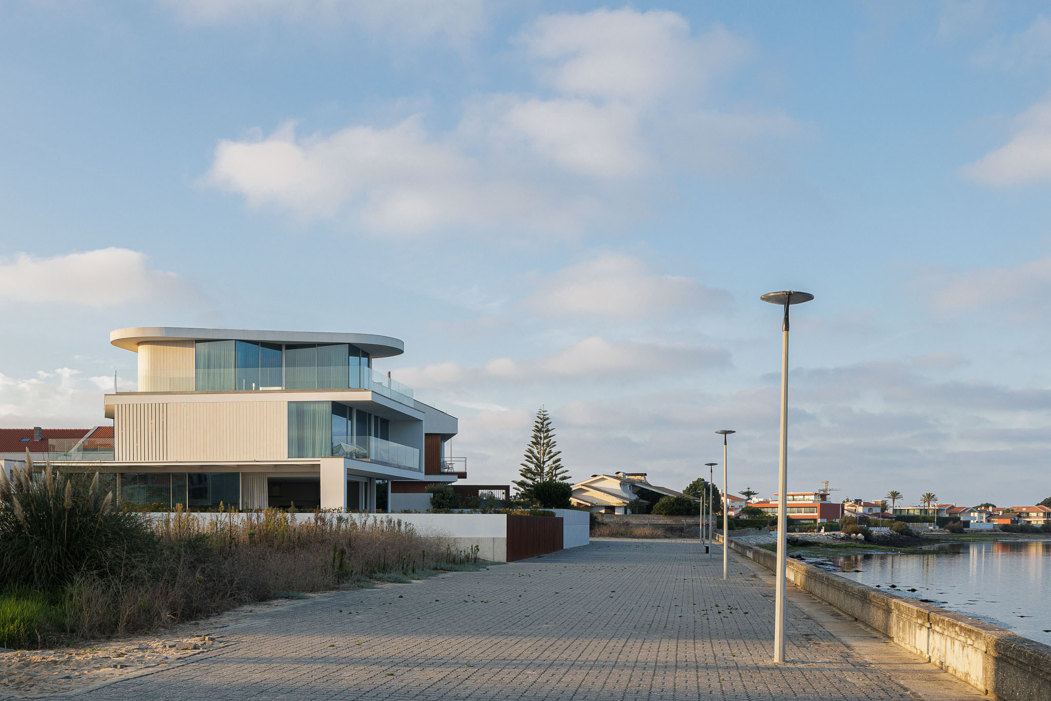 Exterior: Moradia moderna iluminada ao anoitecer, com fachada branca e varandas com guarda em vidro. — Moradia JD2 arquitetura Rui Rosmaninho Arquiteto em Ílhavo