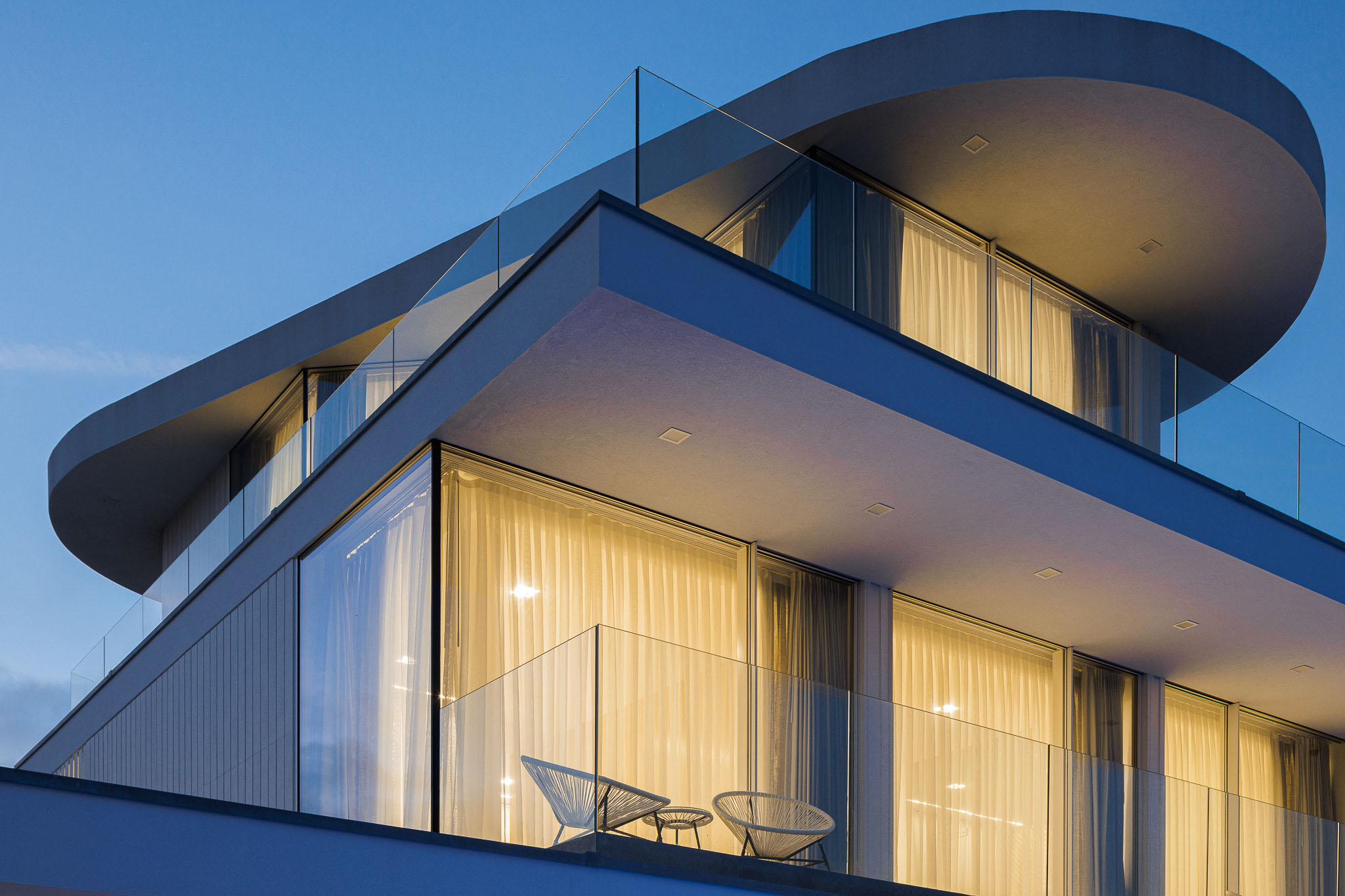 Exterior: Moradia moderna iluminada ao anoitecer, com piscina e vista para a ria. — Moradia JD2 arquitetura Rui Rosmaninho Arquiteto em Ílhavo