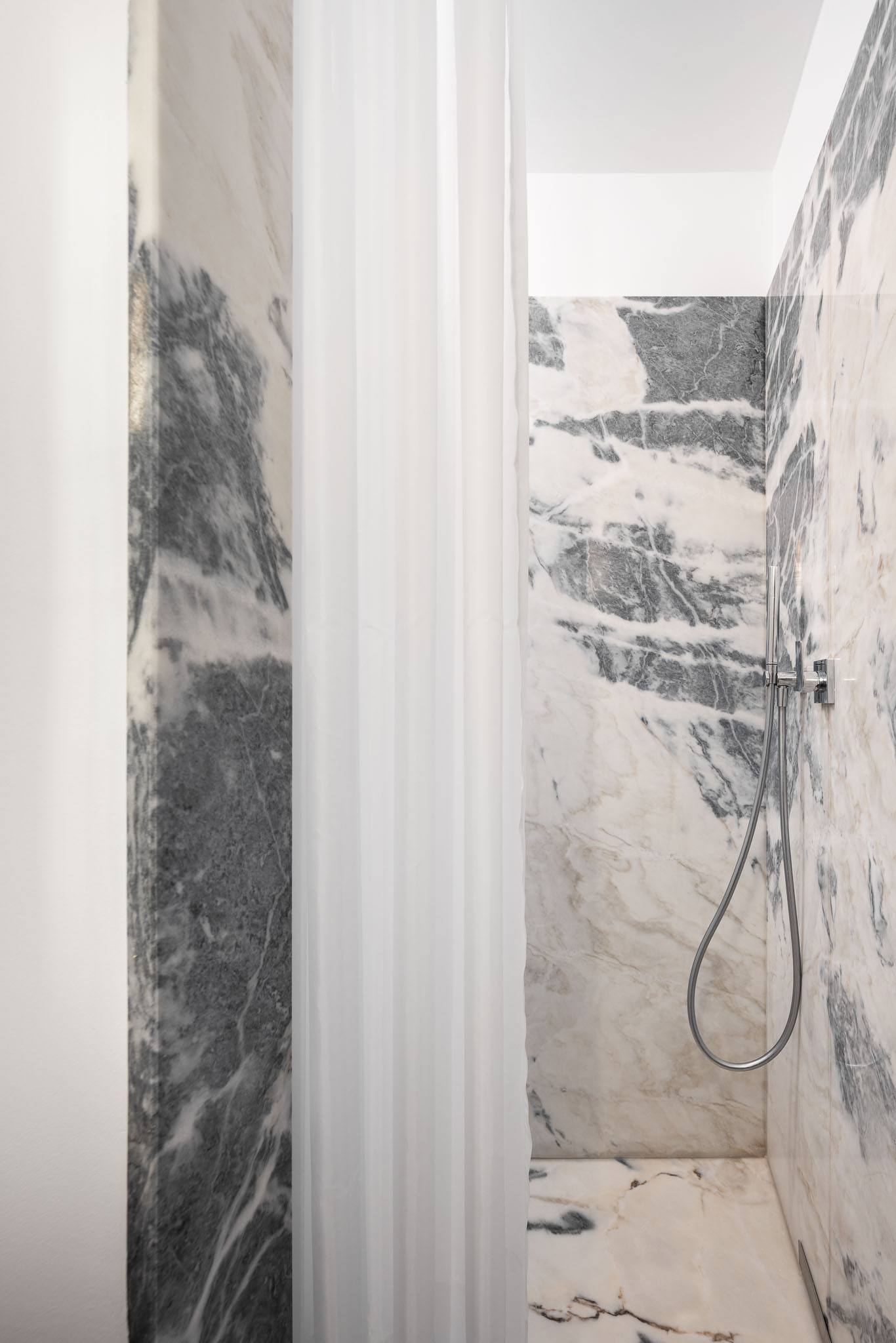Casa de banho: Detalhe do duche com paredes e pavimento em mármore branco com veios cinzentos. Cortina branca translúcida. — Apartamento em Gouveia arquitetura M2Senos Arquitectos em Gouveia