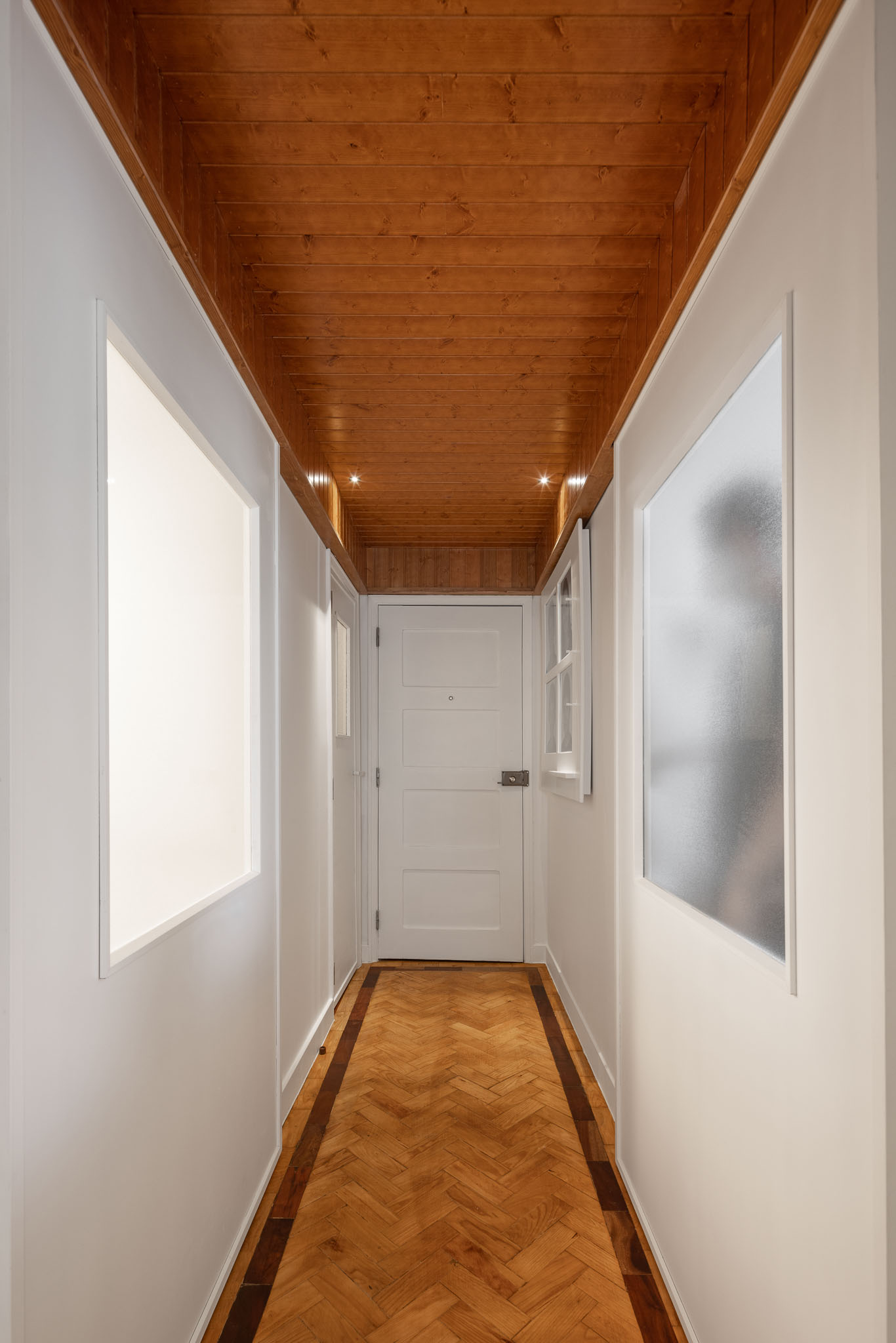 Corredor: Perspectiva do corredor com pavimento em madeira, teto em madeira e paredes brancas. Iluminação embutida no teto. — Apartamento em Gouveia arquitetura M2Senos Arquitectos em Gouveia