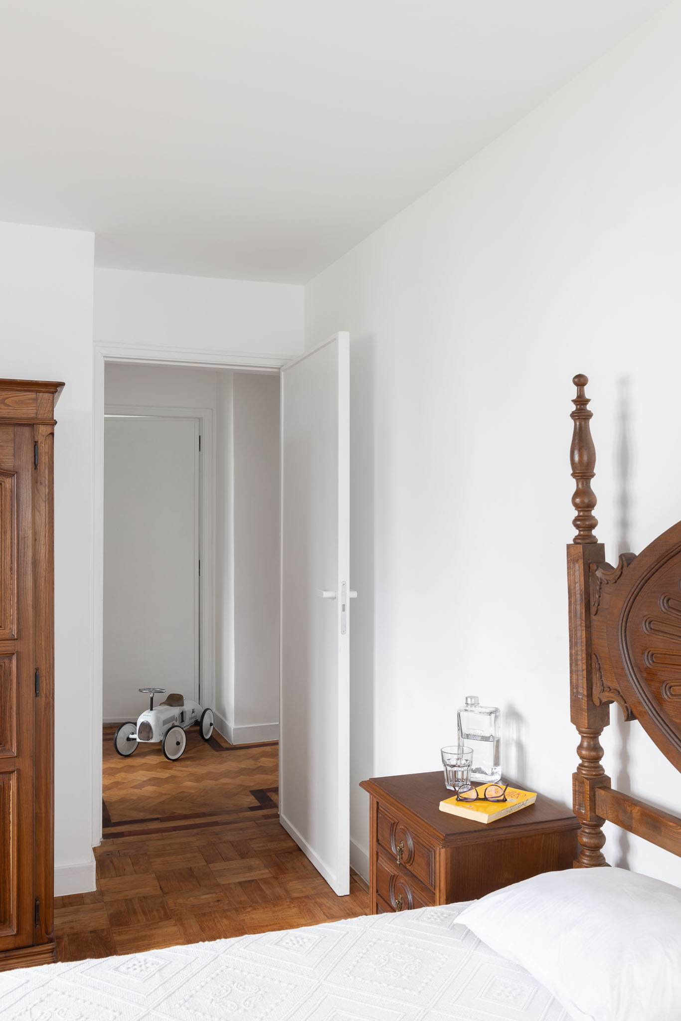 Quarto: Cama de madeira com cabeceira trabalhada, mesa de cabeceira e porta aberta para o corredor com pavimento em madeira. — Apartamento em Gouveia arquitetura M2Senos Arquitectos em Gouveia