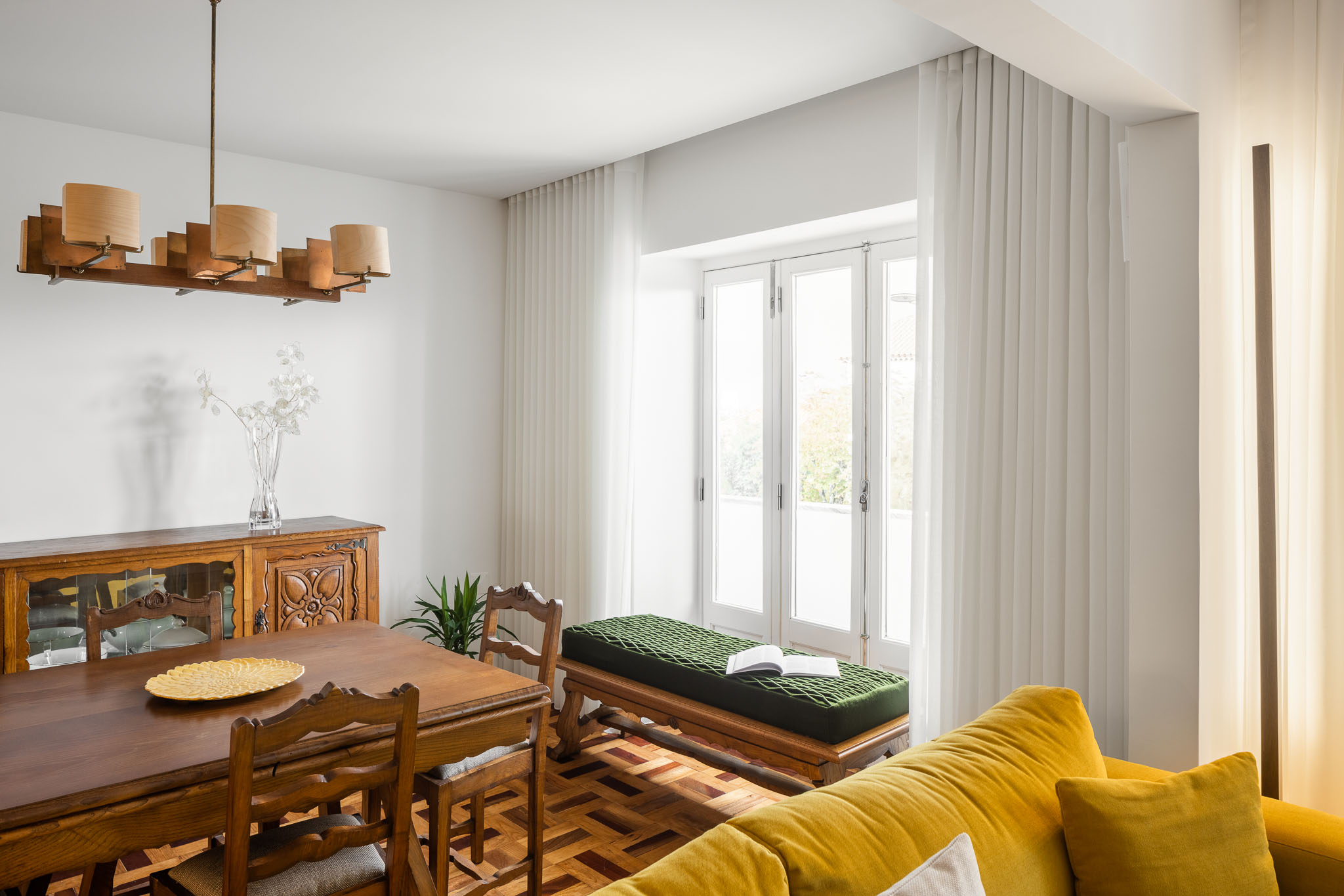 Sala de jantar: Mesa de jantar em madeira com cadeiras, aparador clássico e sofá amarelo em segundo plano. Cortinas brancas. — Apartamento em Gouveia arquitetura M2Senos Arquitectos em Gouveia