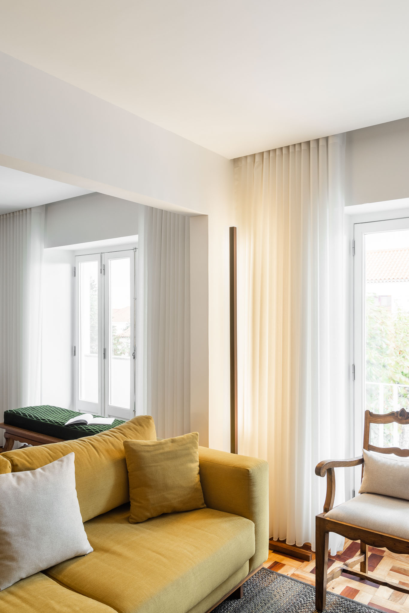 Sala de estar: Sofá amarelo com almofadas, candeeiro de pé minimalista e cortinas brancas. Pavimento em madeira. — Apartamento em Gouveia arquitetura M2Senos Arquitectos em Gouveia
