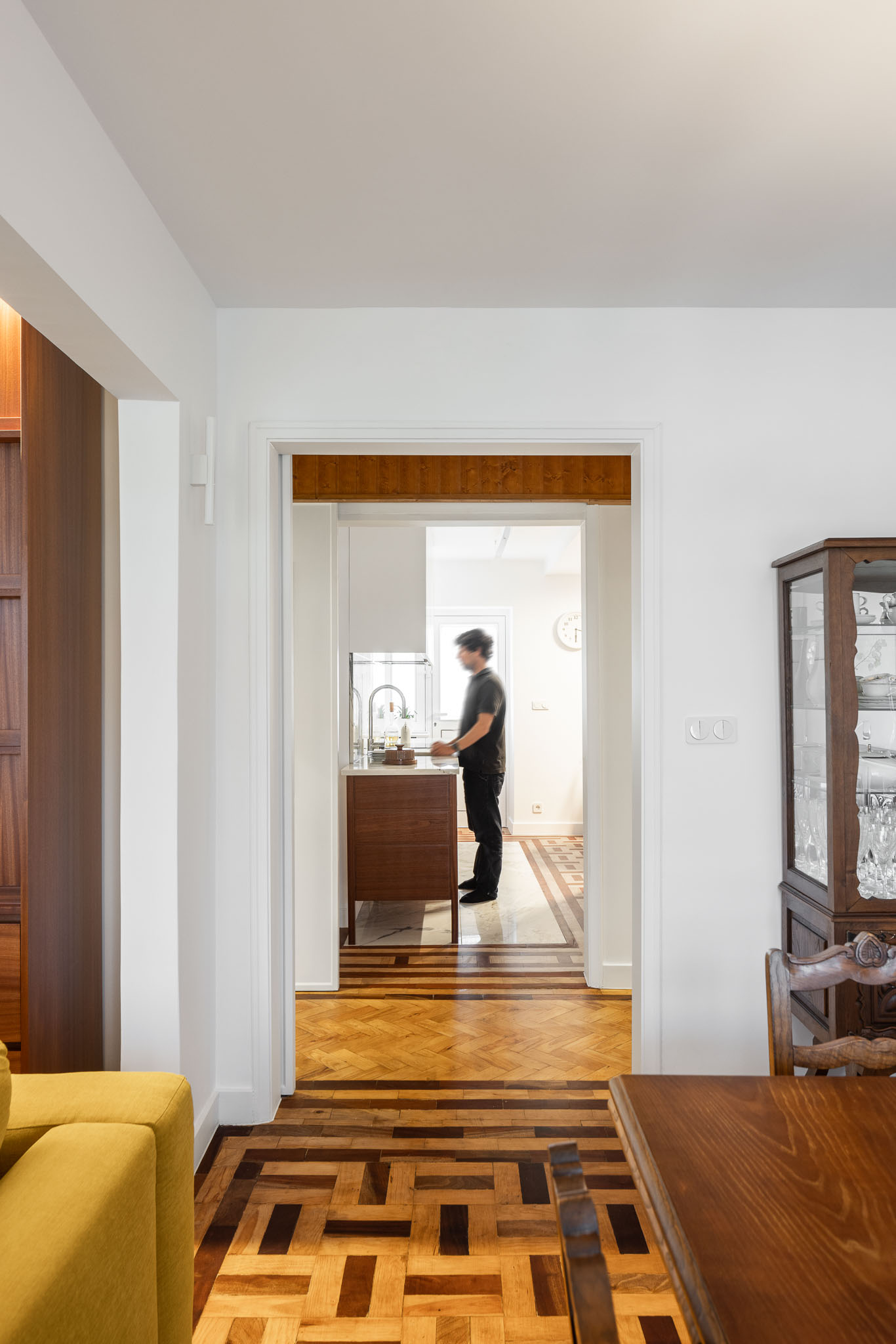 Sala de estar/cozinha: Perspectiva da sala de estar para a cozinha, com pessoa a lavar loiça. Pavimento em madeira. — Apartamento em Gouveia arquitetura M2Senos Arquitectos em Gouveia