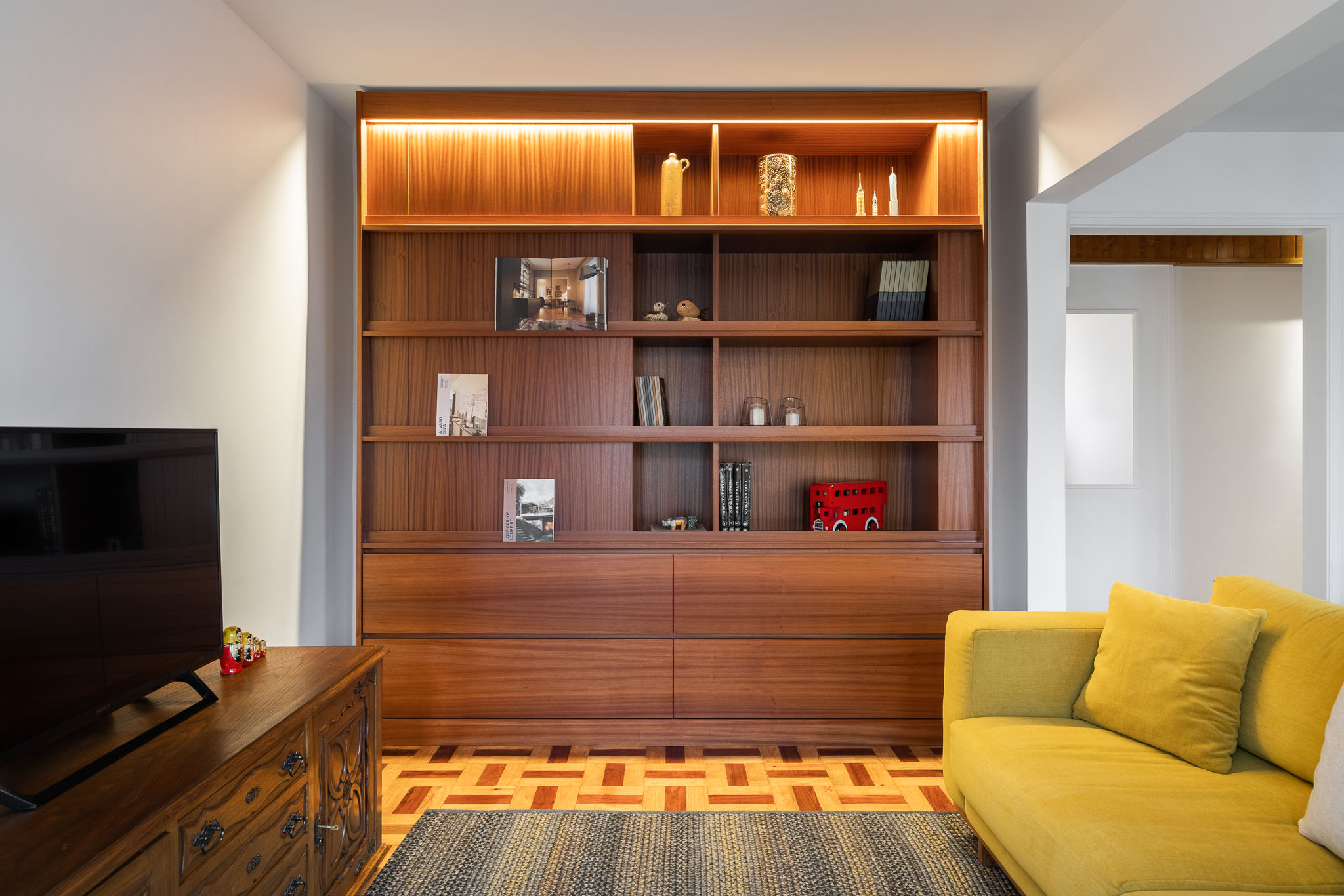 Sala de estar: Estante em madeira com iluminação, televisão e aparador clássico. Sofá amarelo e alcatifa. — Apartamento em Gouveia arquitetura M2Senos Arquitectos em Gouveia