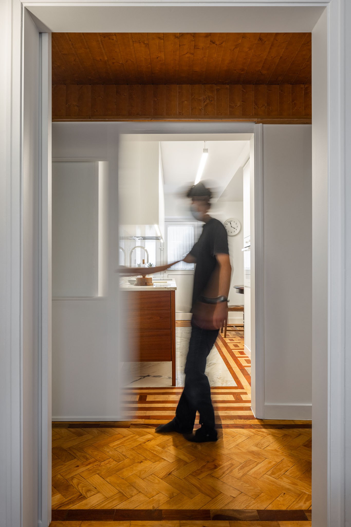 Cozinha: Perspectiva da cozinha a partir do corredor, com pessoa em movimento. Pavimento em madeira e teto em madeira. — Apartamento em Gouveia arquitetura M2Senos Arquitectos em Gouveia