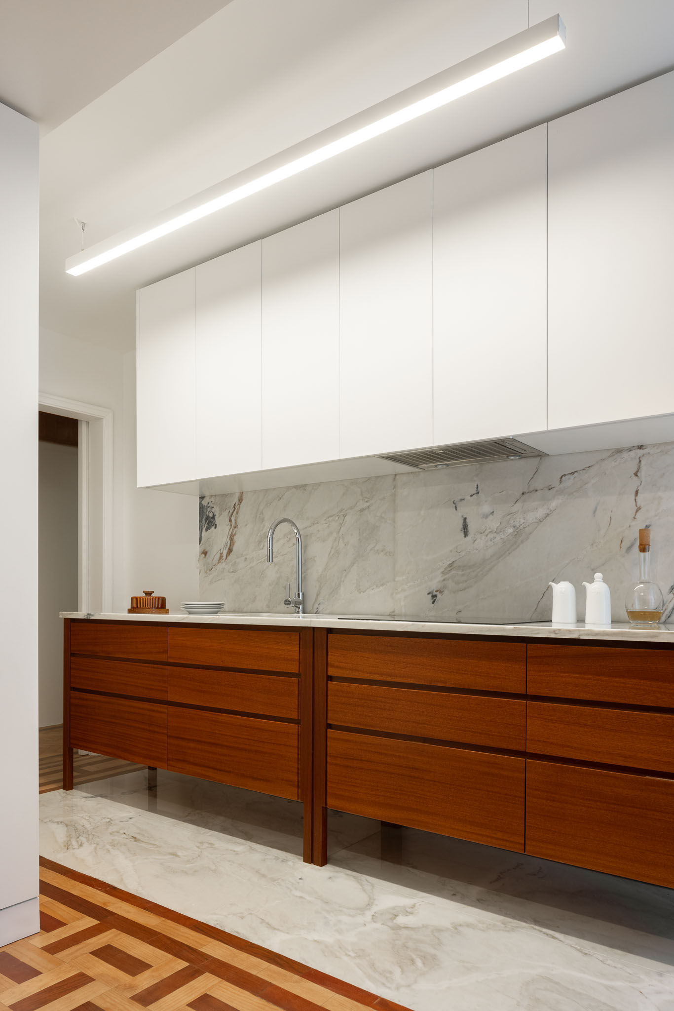 Cozinha: Armários brancos e bancada em mármore com armários em madeira. Pavimento em madeira com detalhe em mármore. — Apartamento em Gouveia arquitetura M2Senos Arquitectos em Gouveia