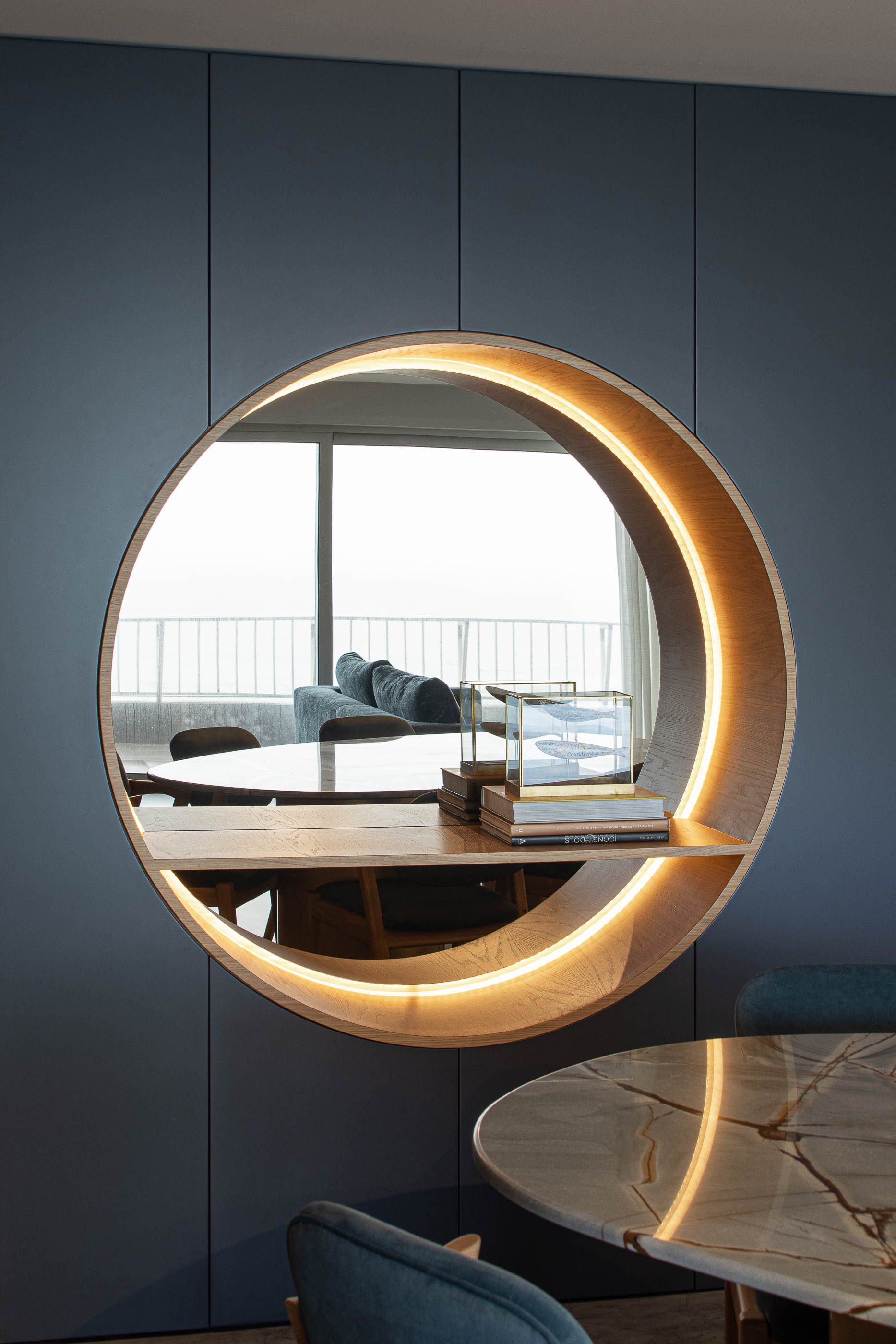 Sala de jantar: Detalhe do espelho circular iluminado, com prateleira em madeira e vista para a sala de estar. — Wave Apartment arquitetura arQB architecture em Póvoa de Varzim