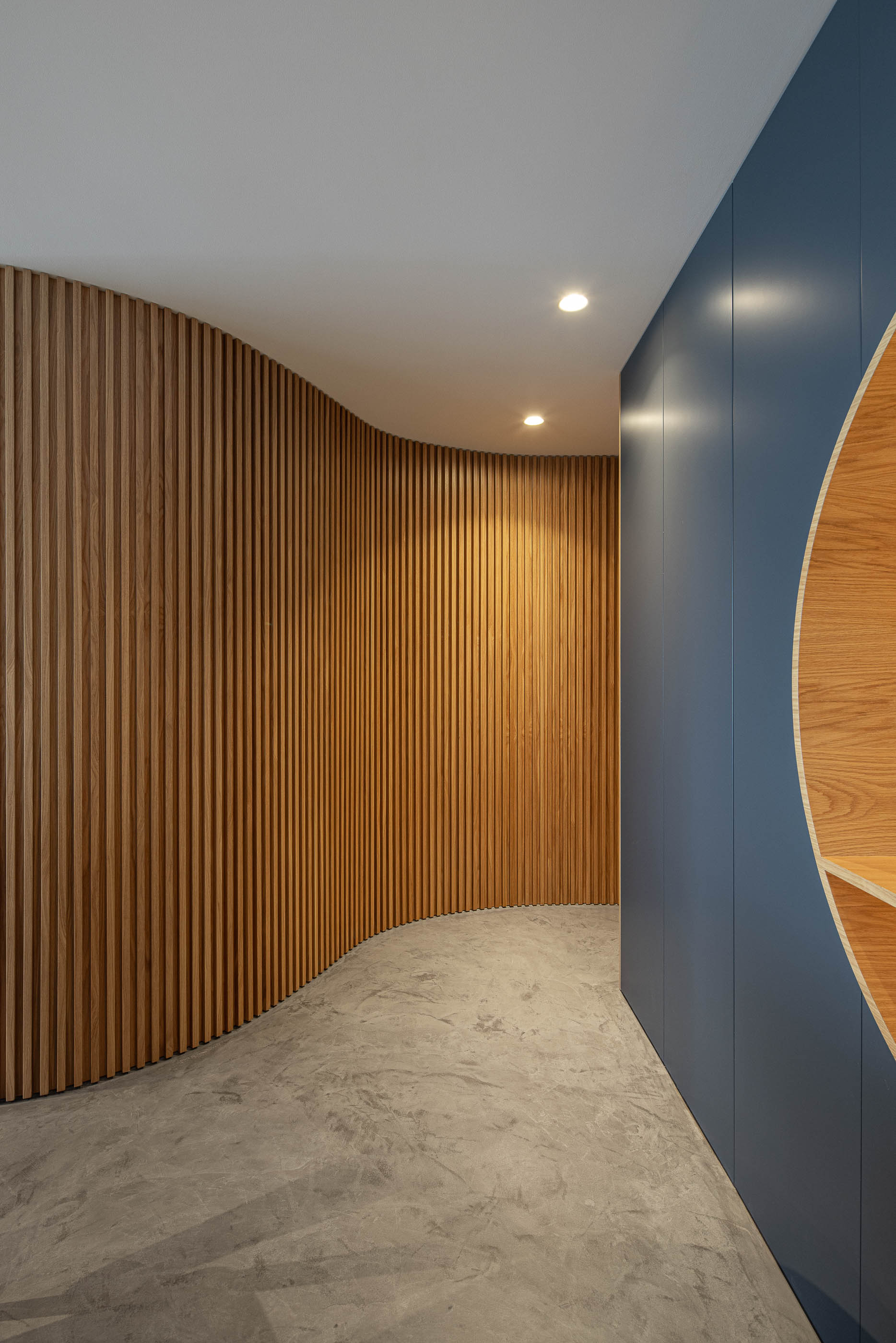 Corredor: Paredes revestidas com ripas de madeira clara, pavimento em cimento afagado e iluminação embutida. — Wave Apartment arquitetura arQB architecture em Póvoa de Varzim