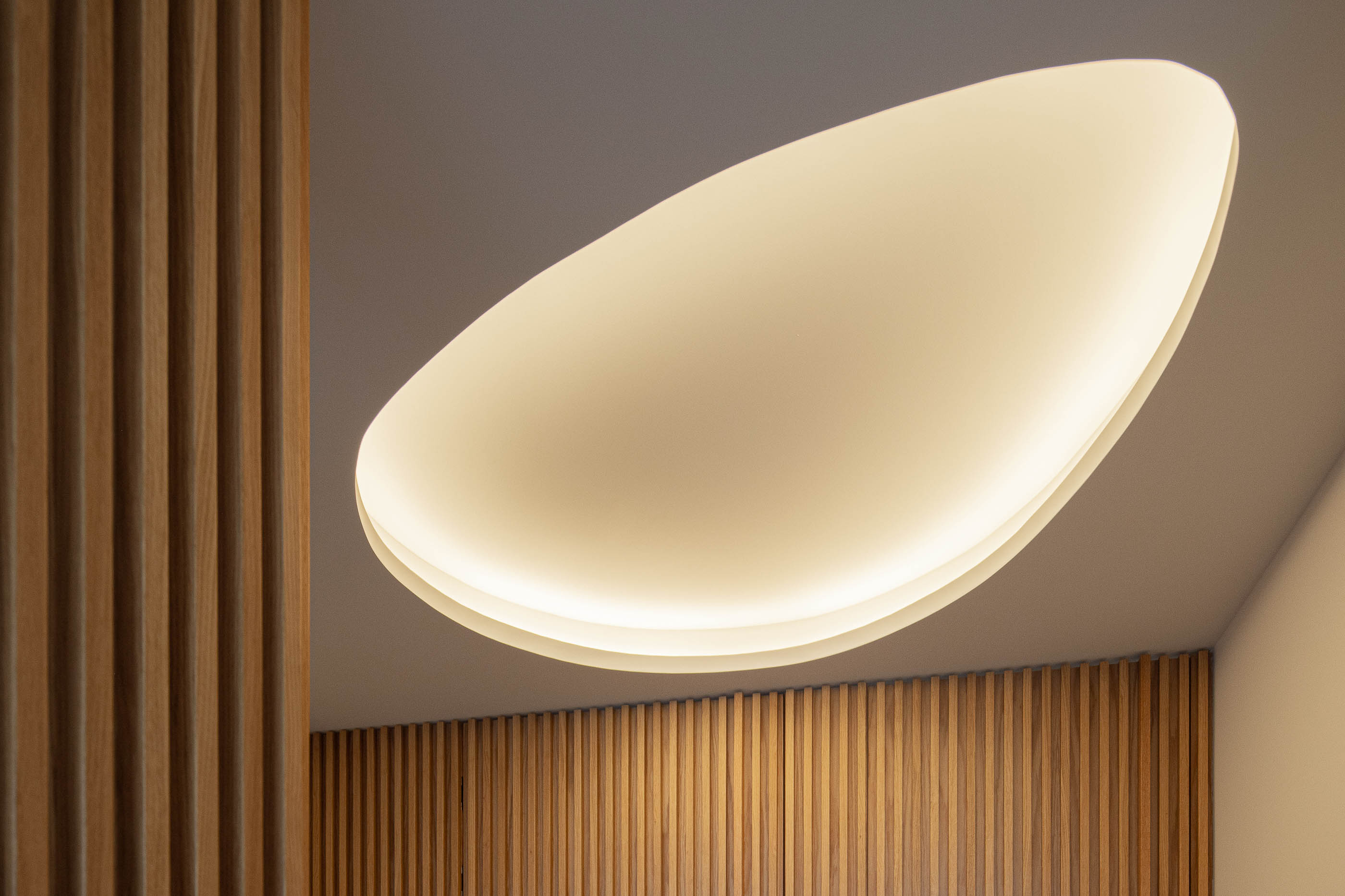 Corredor: Detalhe do teto com candeeiro oval e paredes revestidas com ripas de madeira clara. — Wave Apartment arquitetura arQB architecture em Póvoa de Varzim