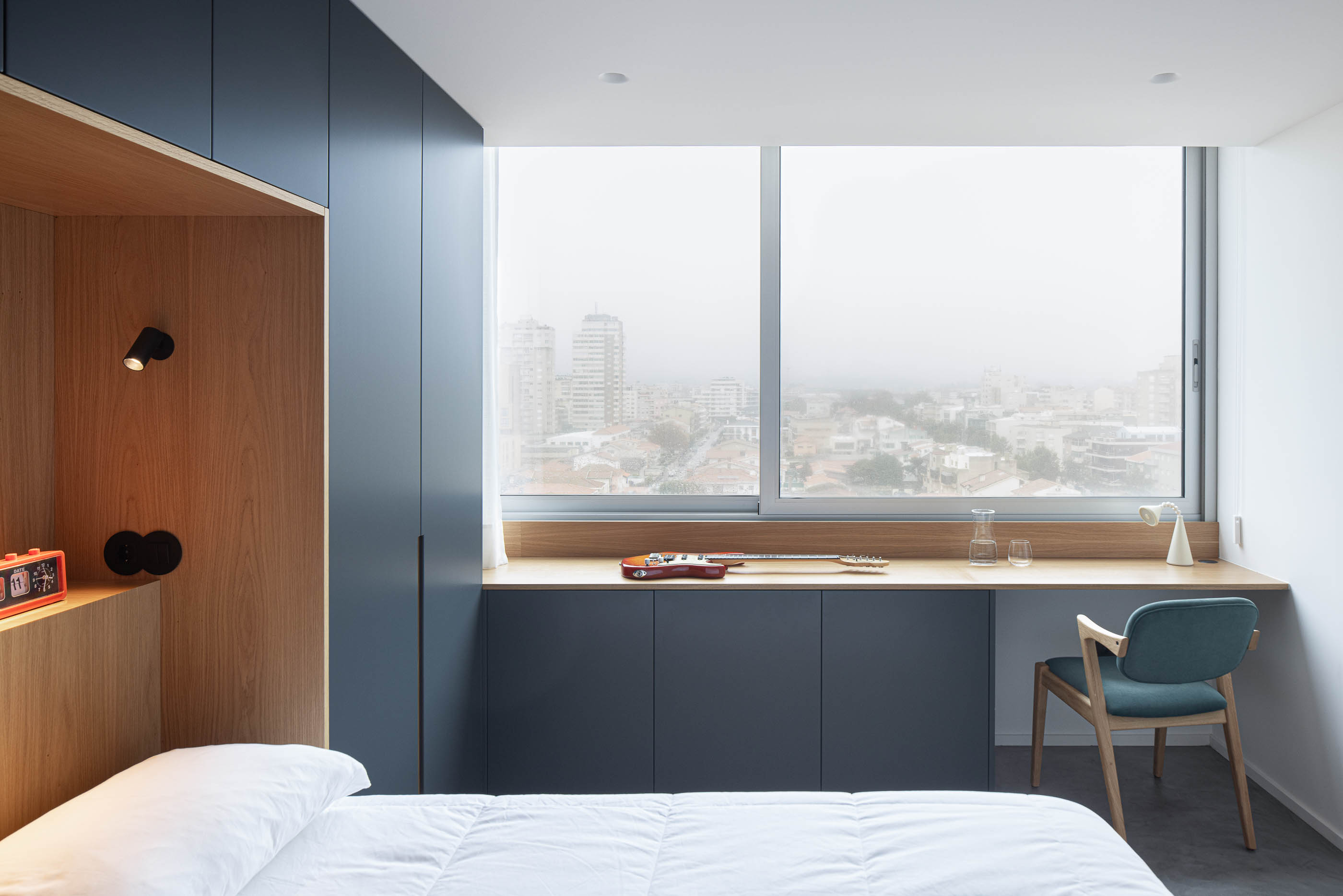 Quarto: Cama com cabeceira em madeira clara e candeeiros de parede pretos embutidos no nicho. — Wave Apartment arquitetura arQB architecture em Póvoa de Varzim