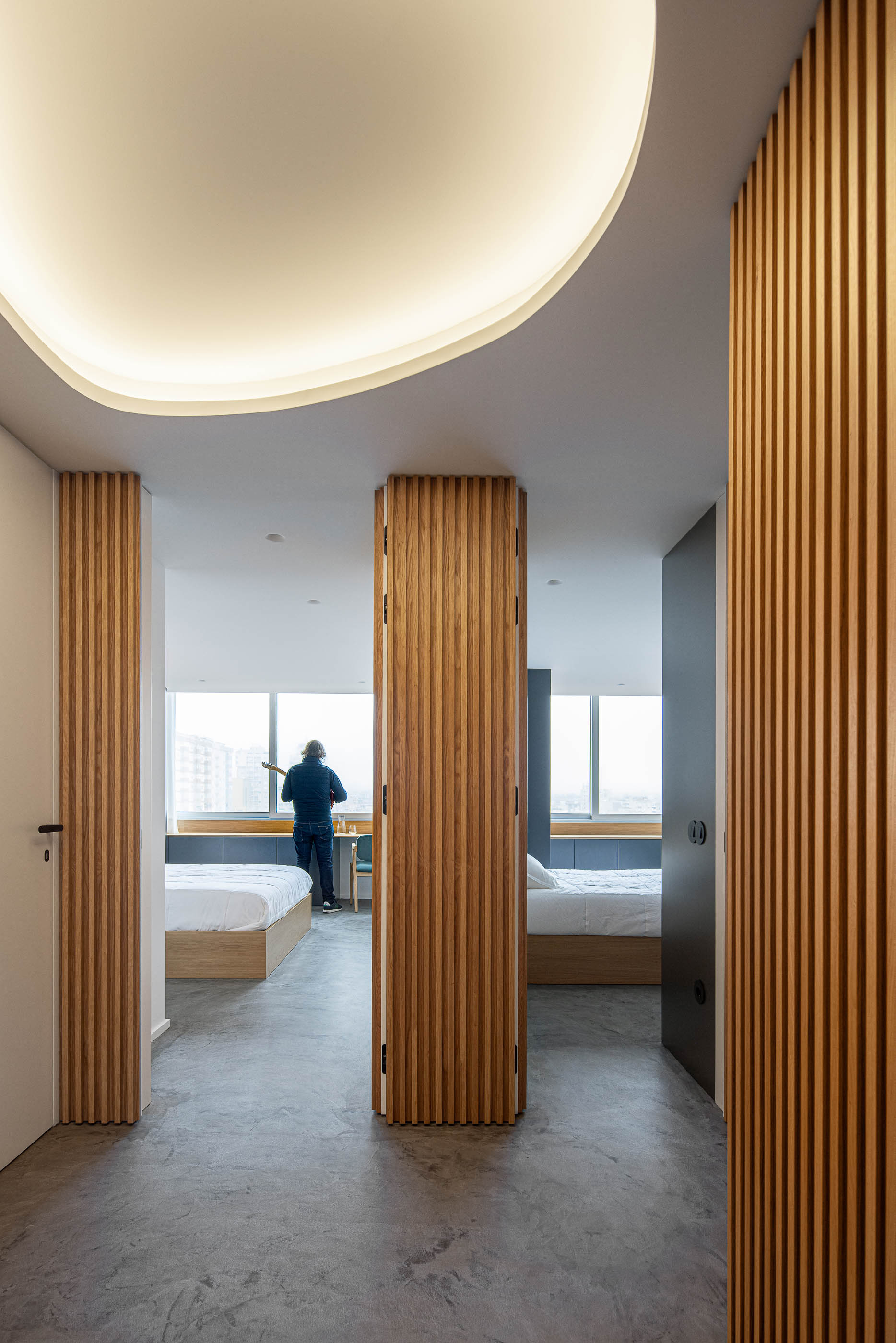 Quarto: Vista da janela com secretária, cadeira e vista para a cidade, armário azul e cabeceira em madeira. — Wave Apartment arquitetura arQB architecture em Póvoa de Varzim