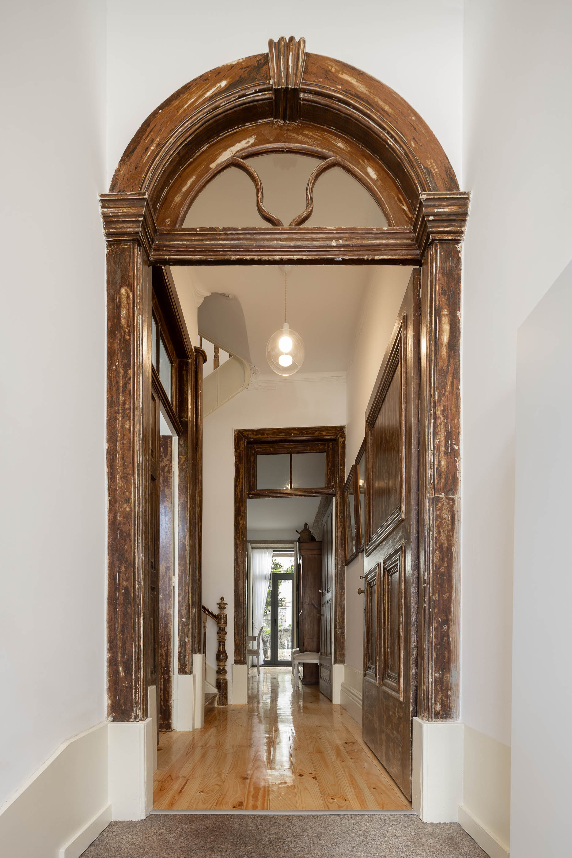 Hall de entrada com porta antiga em madeira trabalhada, pavimento em madeira clara e candeeiro suspenso moderno. — Casa Cedofeita arquitetura Paulo Moreira Architectures em Porto