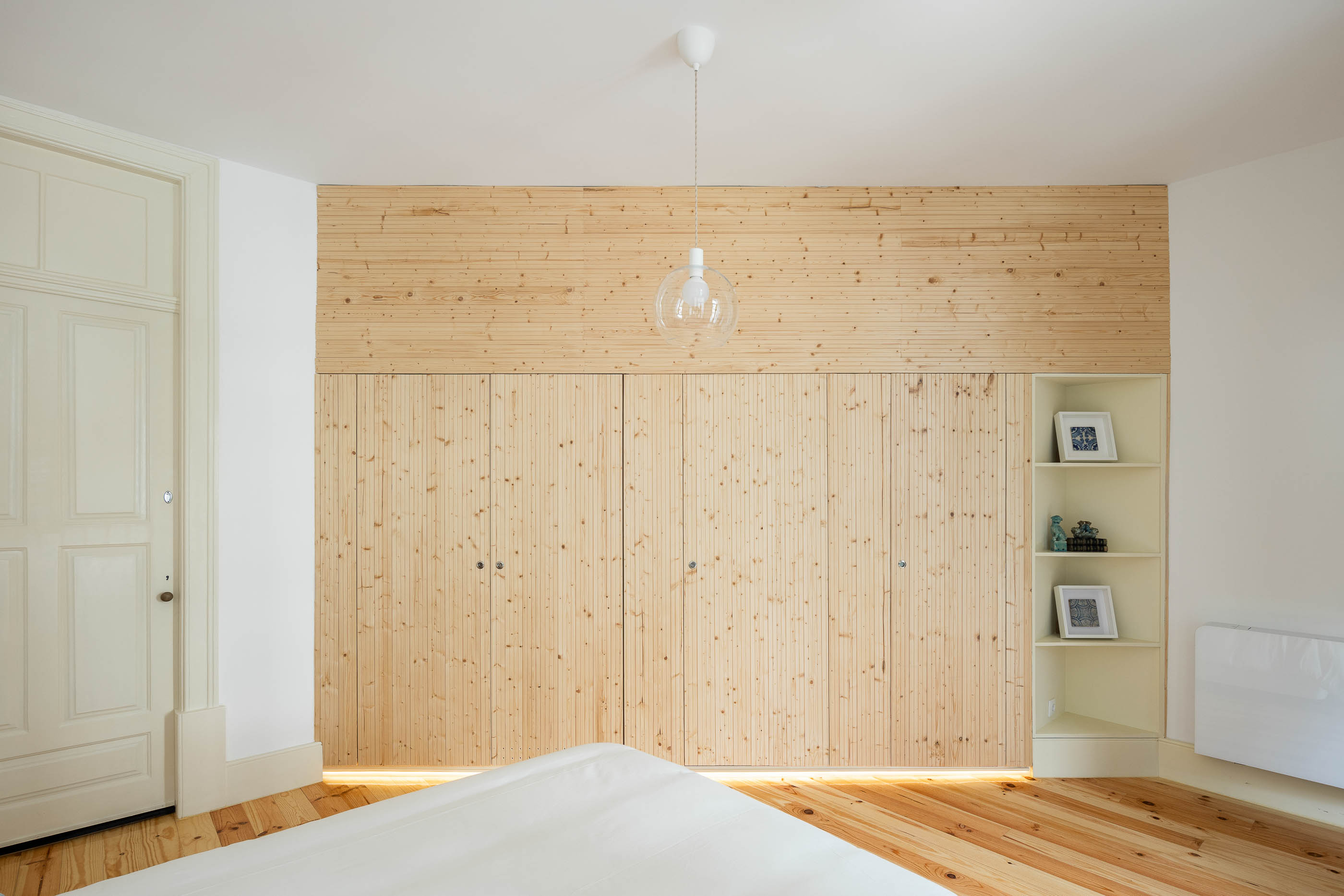 Quarto de dormir com roupeiro em madeira clara, prateleiras embutidas e pavimento em madeira. — Casa Cedofeita arquitetura Paulo Moreira Architectures em Porto