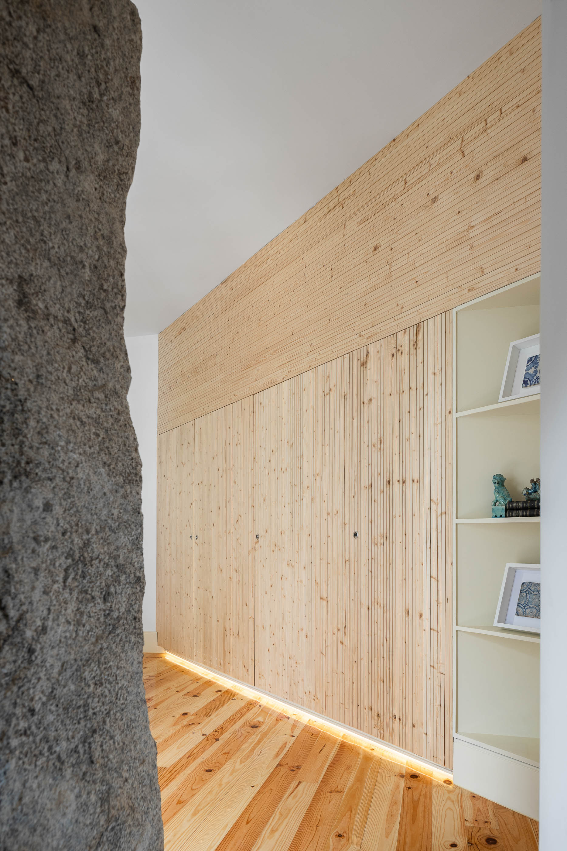 Quarto de dormir com parede em pedra original, roupeiro em madeira clara e prateleiras embutidas. — Casa Cedofeita arquitetura Paulo Moreira Architectures em Porto
