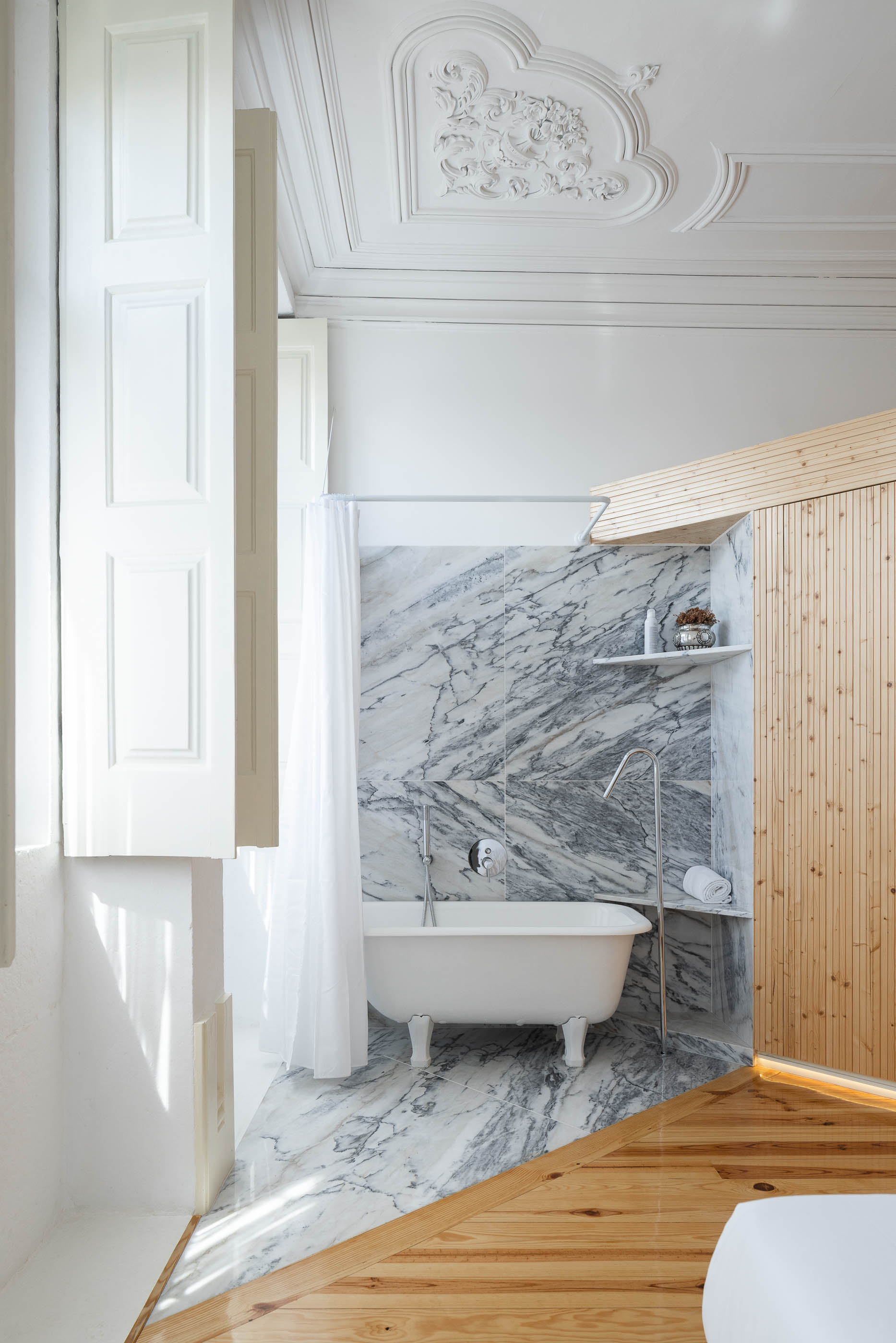 Casa de banho com banheira clássica, revestimento em mármore e roupeiro em madeira clara. — Casa Cedofeita arquitetura Paulo Moreira Architectures em Porto