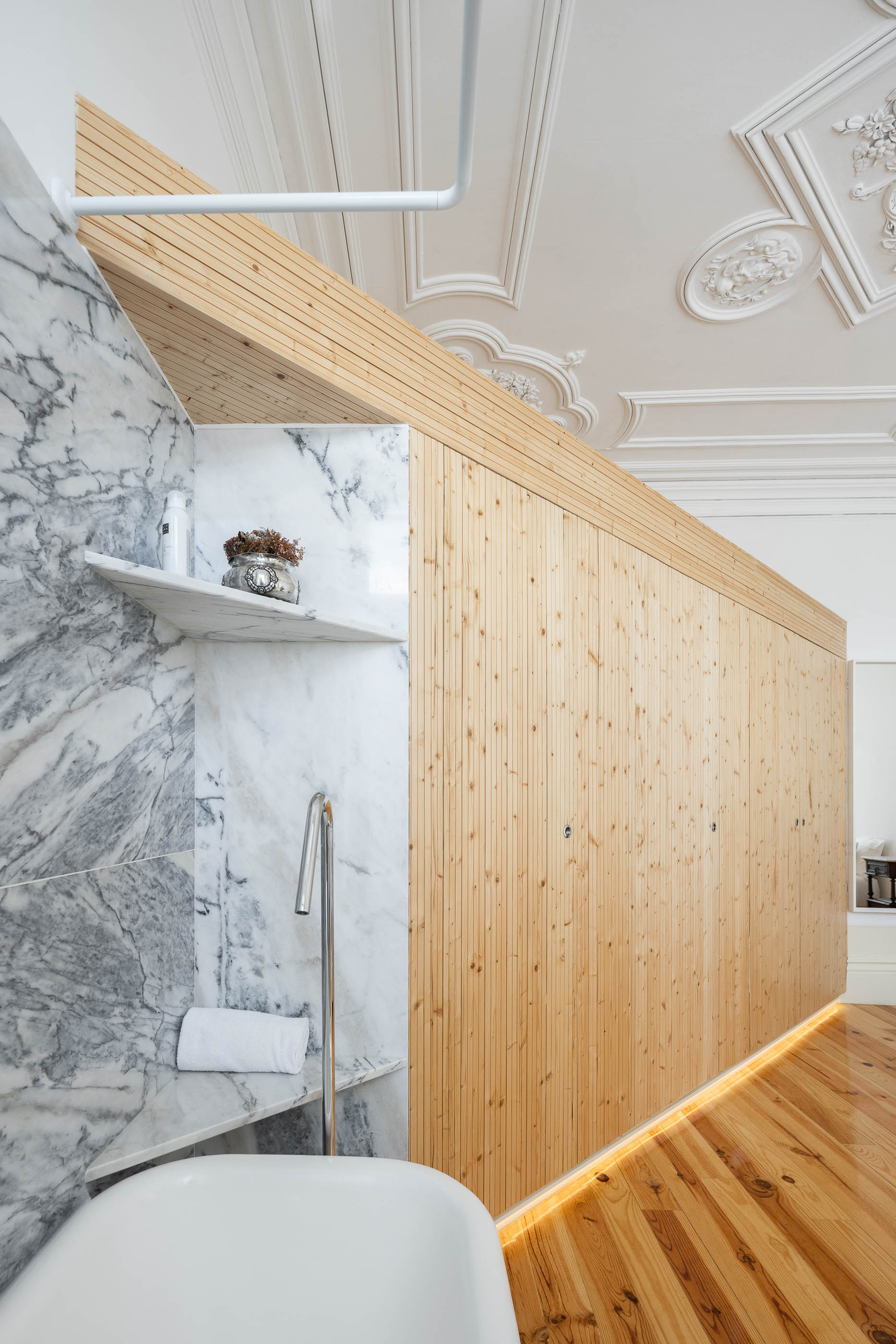 Casa de banho com roupeiro em madeira clara, prateleiras em mármore e banheira branca visível. — Casa Cedofeita arquitetura Paulo Moreira Architectures em Porto