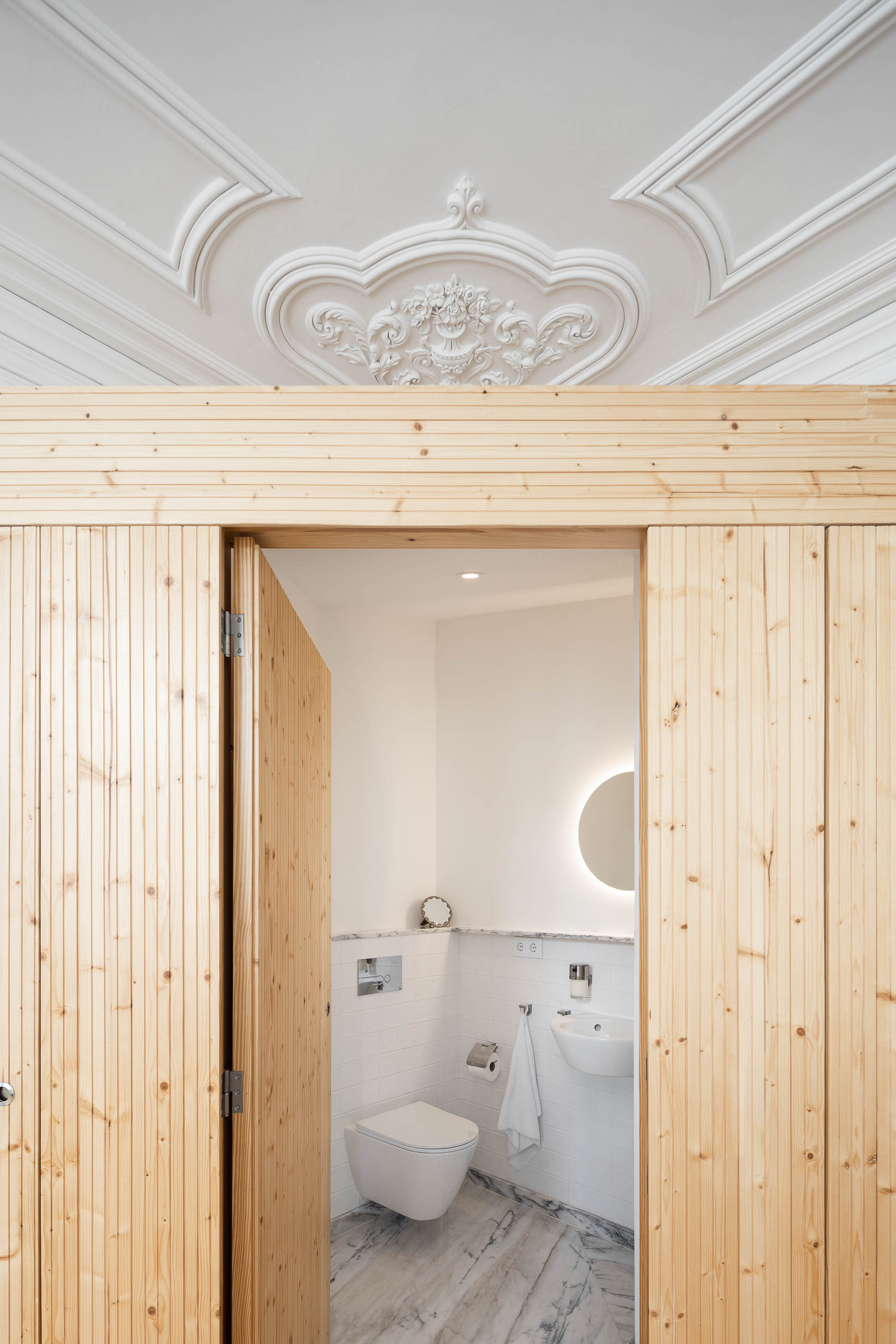 Casa de banho social com sanita suspensa, lavatório branco e roupeiro em madeira clara. — Casa Cedofeita arquitetura Paulo Moreira Architectures em Porto
