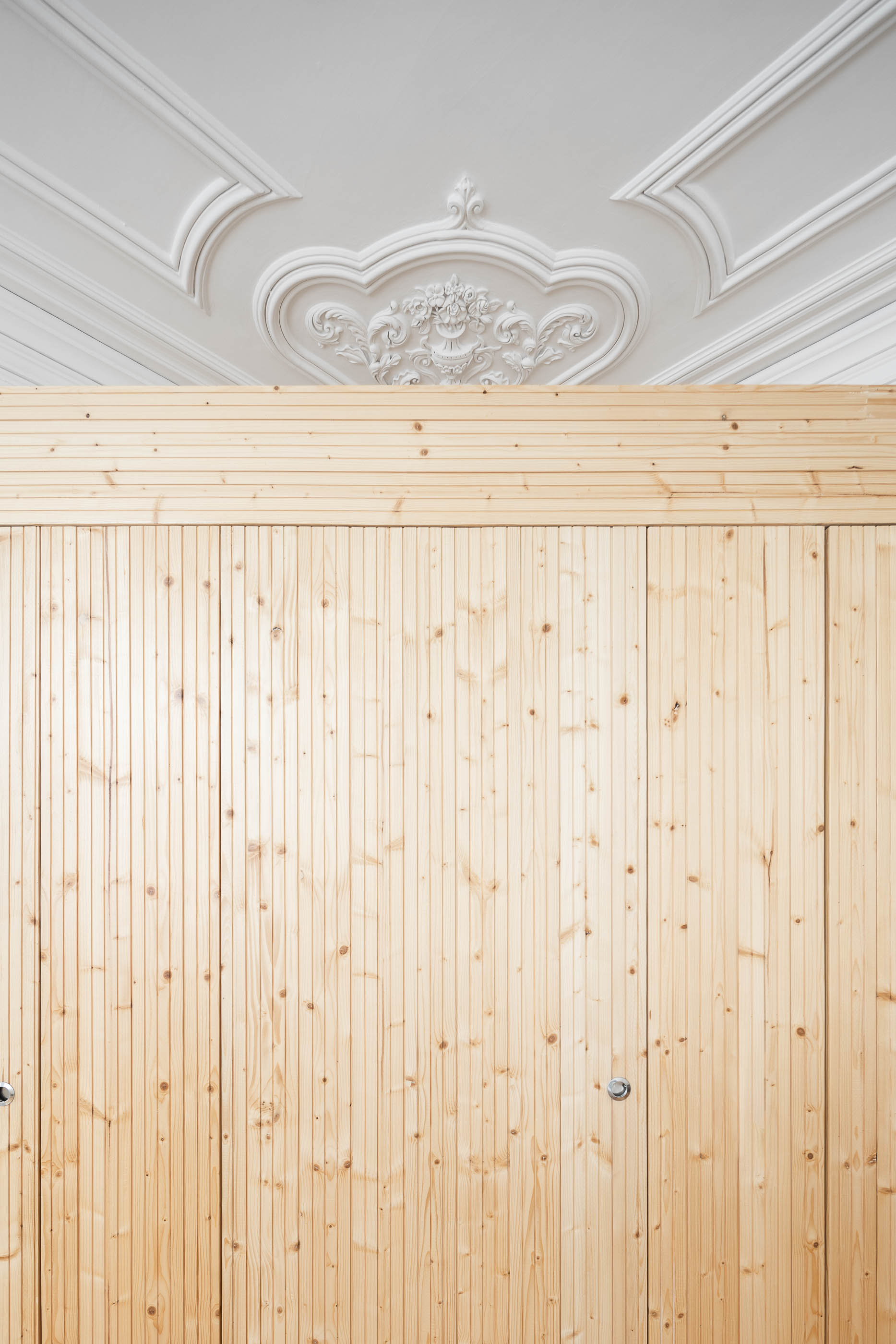 Detalhe do roupeiro em madeira clara com portas de correr e teto com molduras decorativas. — Casa Cedofeita arquitetura Paulo Moreira Architectures em Porto