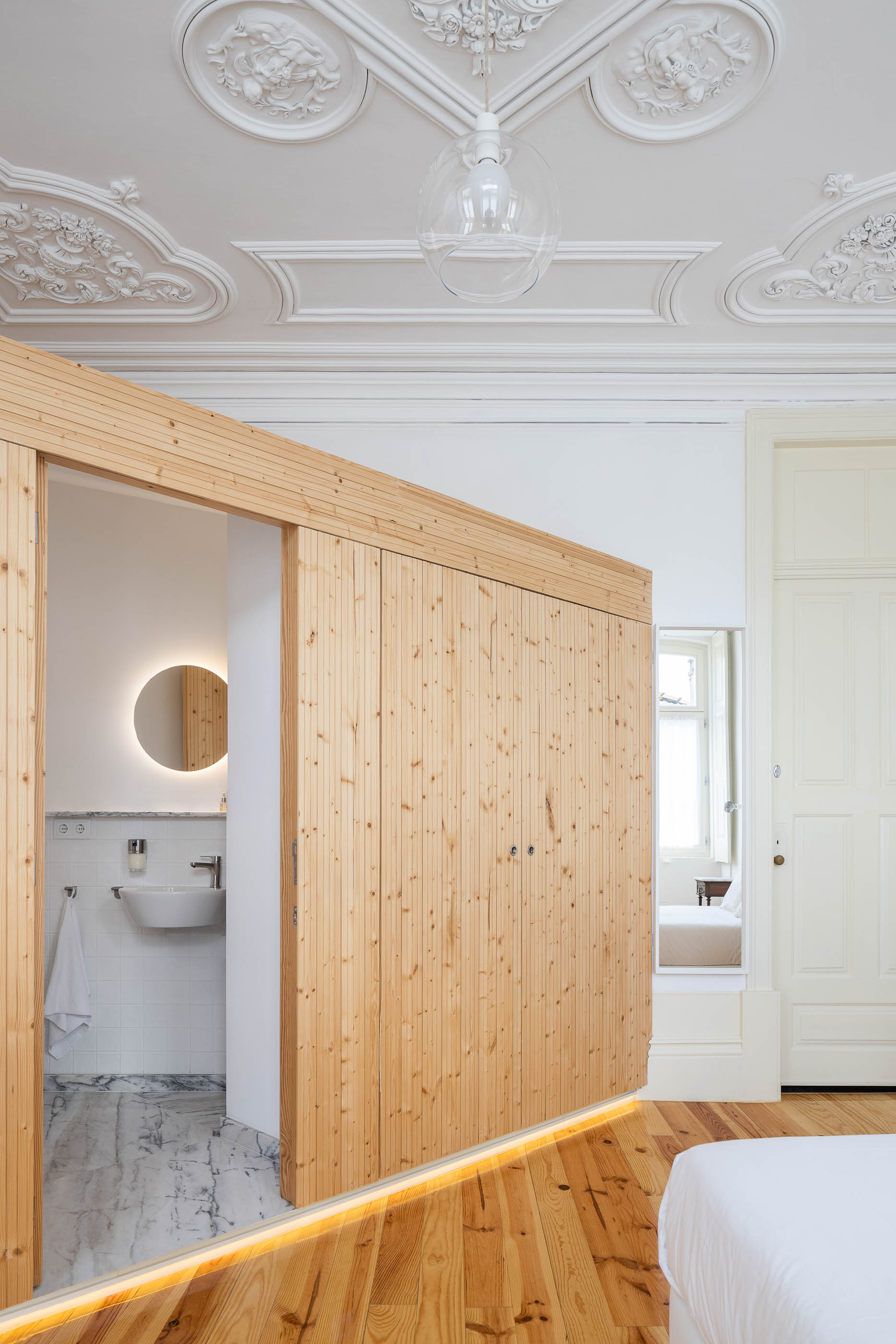 Quarto de dormir com roupeiro em madeira clara, casa de banho adjacente e pavimento em madeira. — Casa Cedofeita arquitetura Paulo Moreira Architectures em Porto