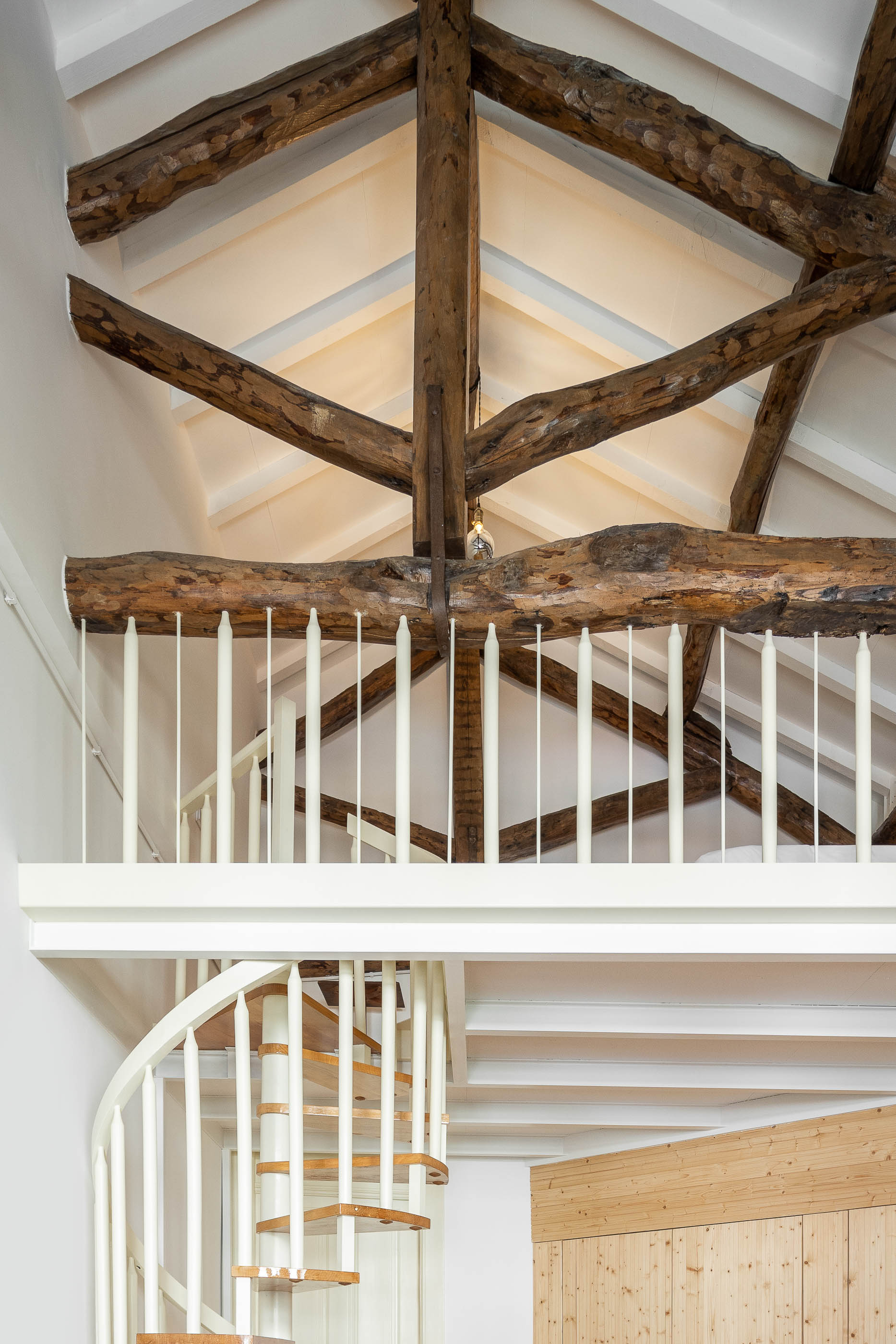 Mezzanine com vigas de madeira expostas, escada em caracol e guarda-corpo branco. — Casa Cedofeita arquitetura Paulo Moreira Architectures em Porto