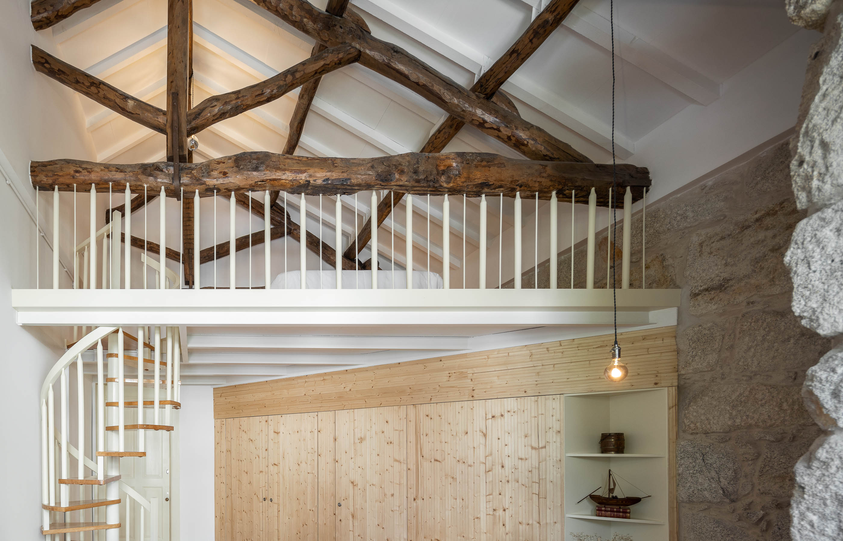 Mezzanine com cama, vigas de madeira expostas e parede em pedra original. — Casa Cedofeita arquitetura Paulo Moreira Architectures em Porto