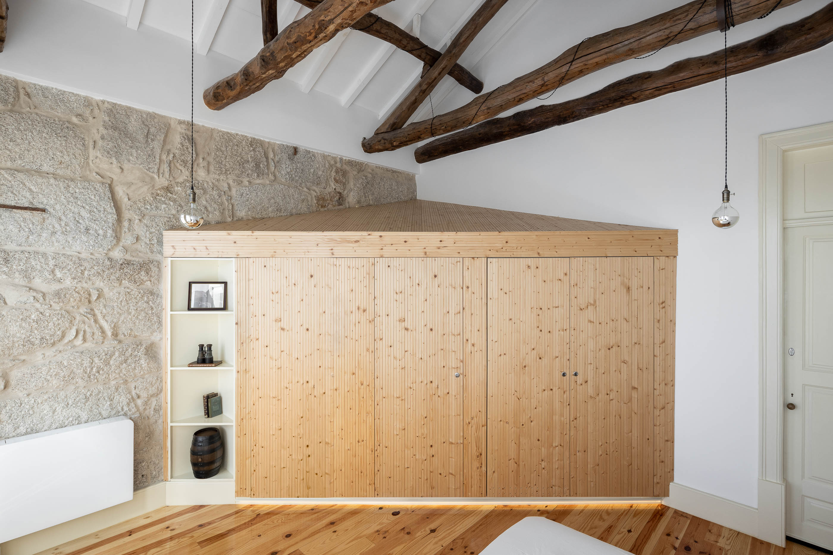 Quarto de dormir com parede em pedra original, roupeiro em madeira clara e pavimento em madeira. — Casa Cedofeita arquitetura Paulo Moreira Architectures em Porto
