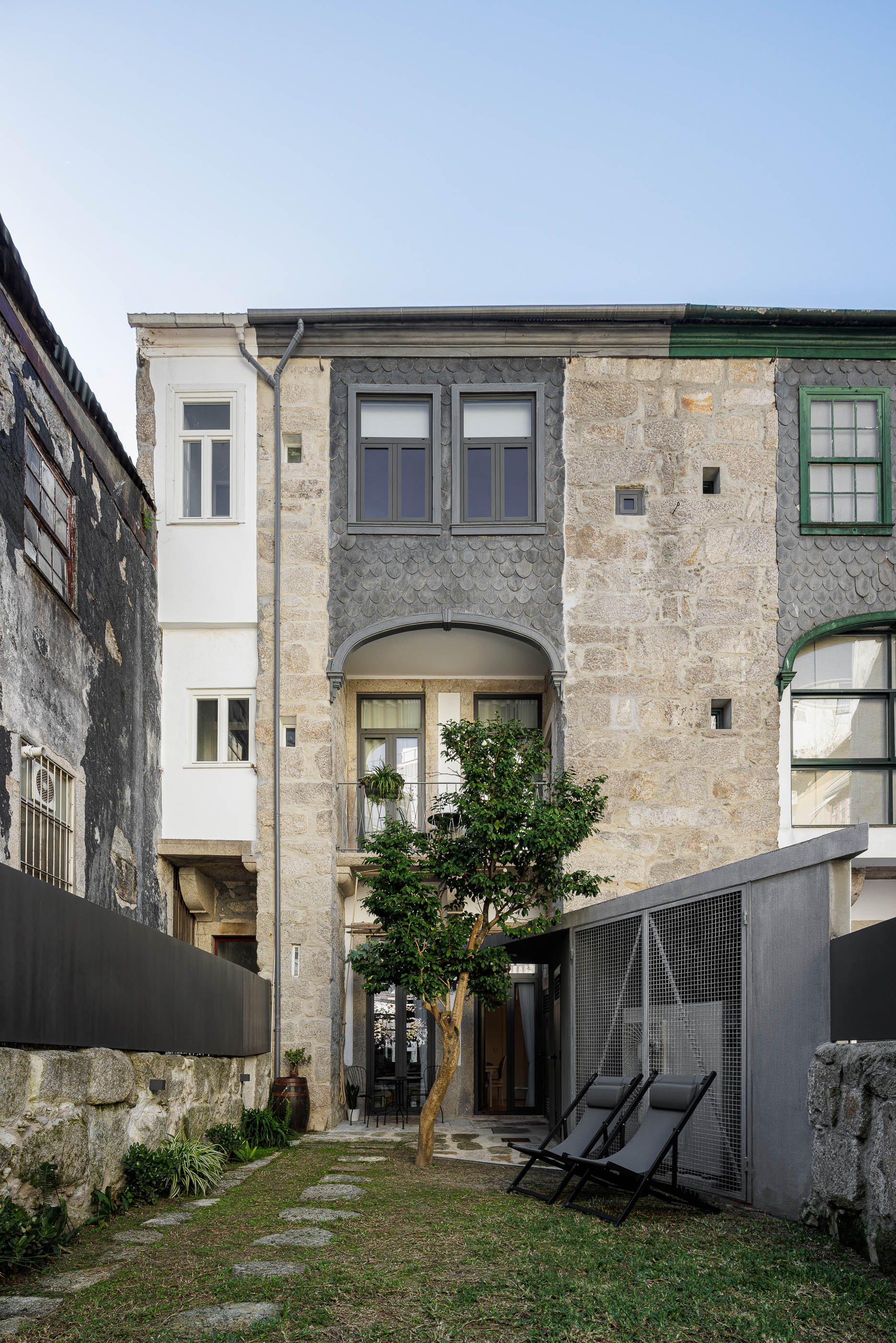 Fachada posterior da casa com jardim, cadeiras de exterior e revestimento em pedra original. — Casa Cedofeita arquitetura Paulo Moreira Architectures em Porto