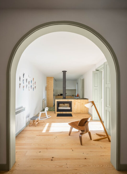 Sala de estar: Arco em verde claro para a cozinha, lareira moderna, cadeira de design e pavimento em madeira. — Casa em Bencanta arquitetura Filipe Pina Arquitectura em Coimbra