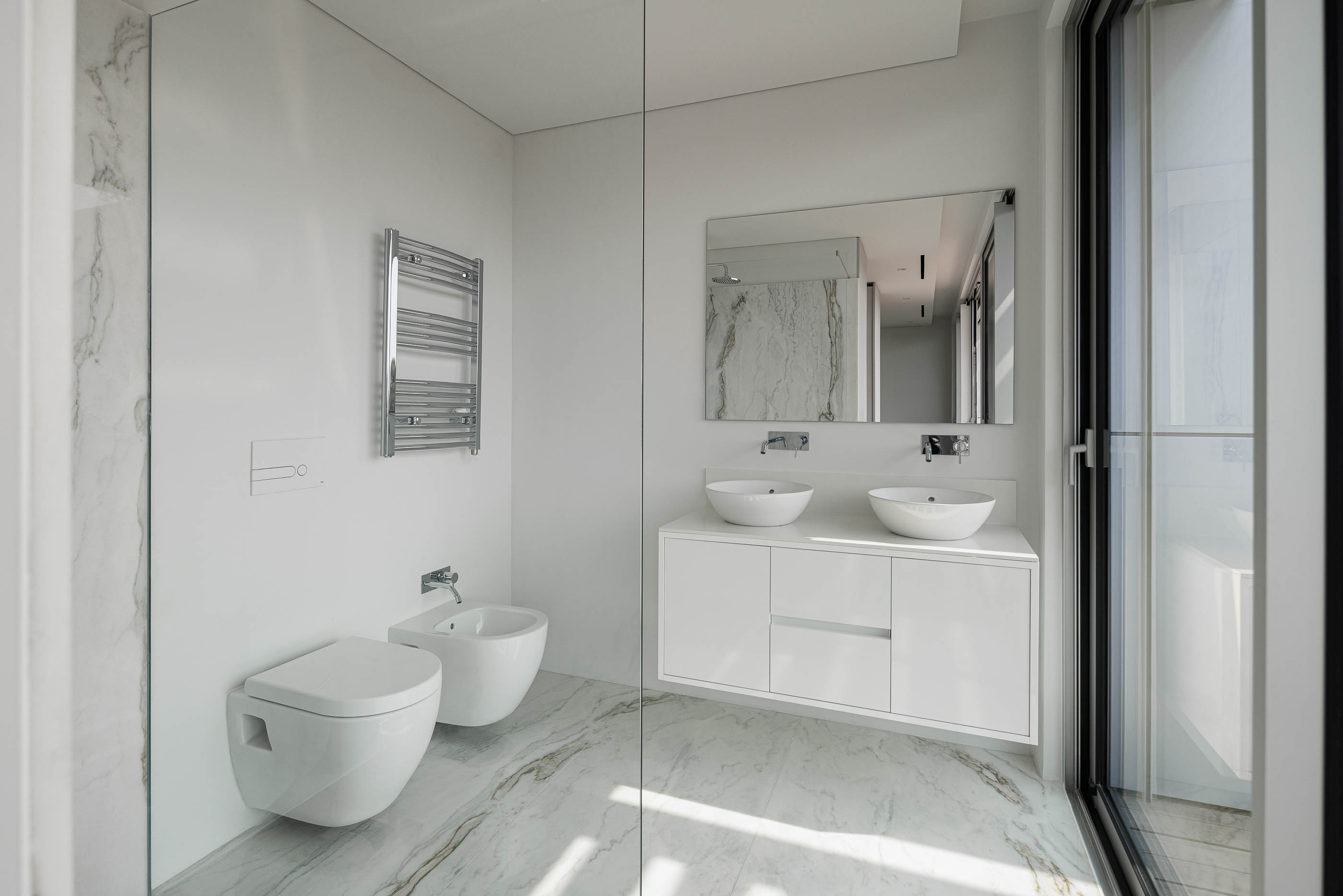 Casa de banho: Revestimento em mármore branco, lavatório duplo de pousar e sanitários suspensos. — Evolution Apartments Housing arquitetura António Paulo Marques, Arquiteto e Associados em Matosinhos