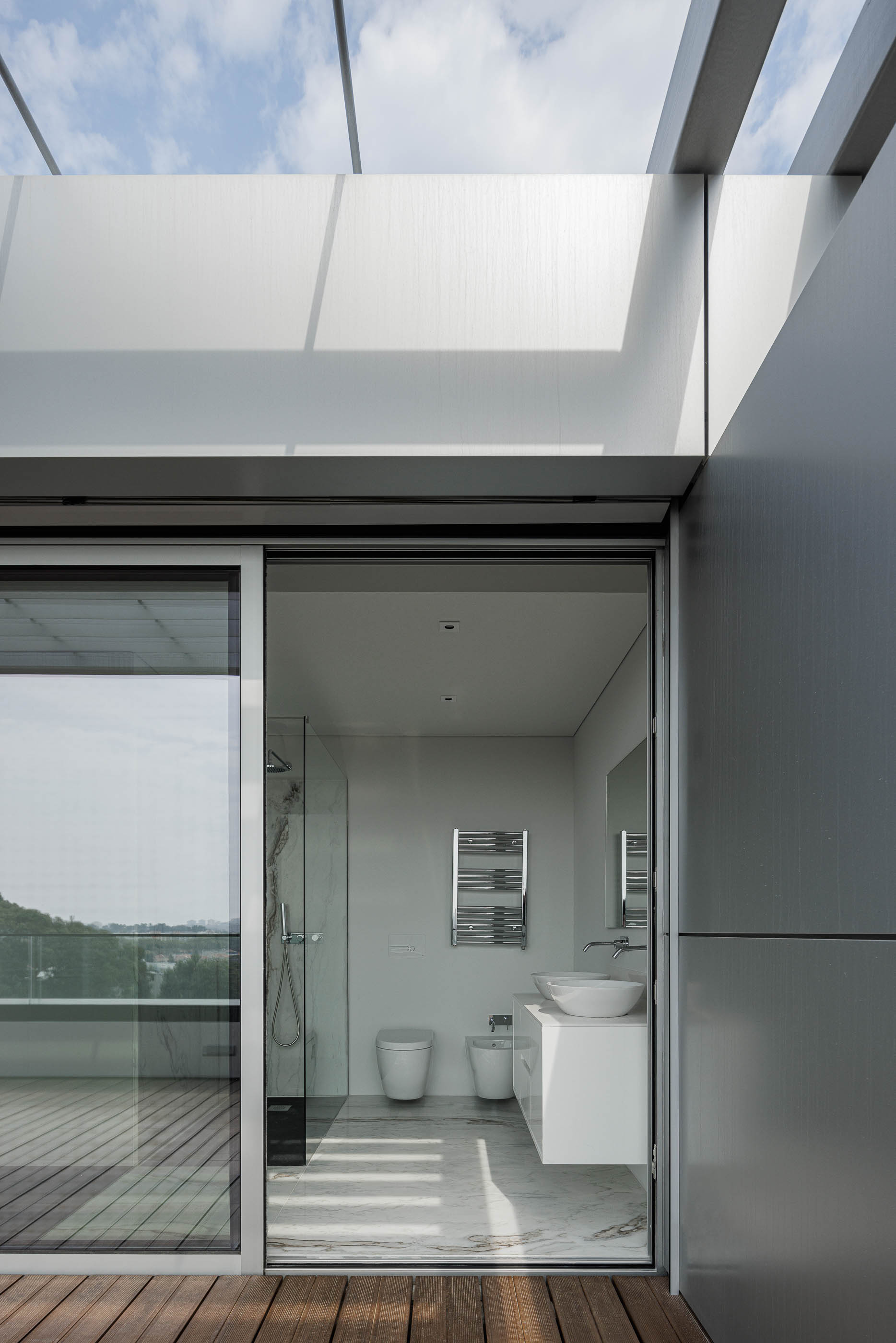 Terraço: Pavimento em madeira que continua para a casa de banho, com revestimento em mármore. — Evolution Apartments Housing arquitetura António Paulo Marques, Arquiteto e Associados em Matosinhos