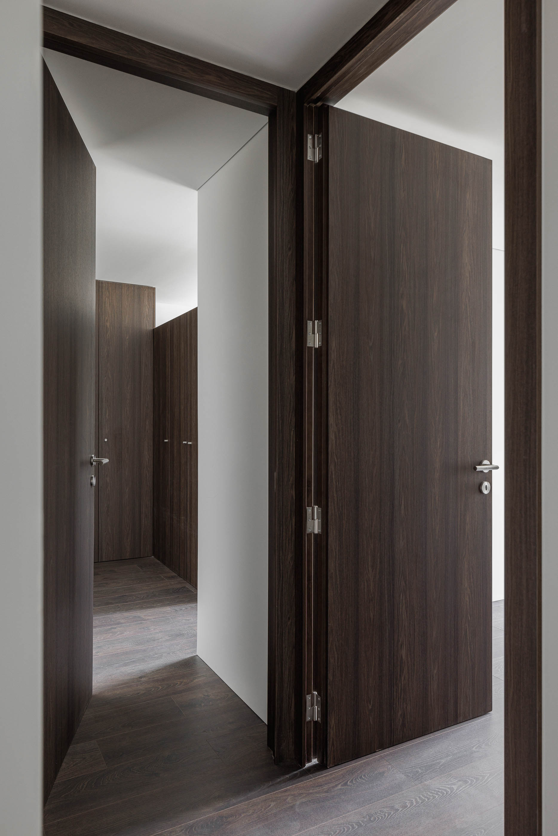 Corredor: Portas em madeira escura e pavimento em madeira, com armários embutidos. — Evolution Apartments Housing arquitetura António Paulo Marques, Arquiteto e Associados em Matosinhos