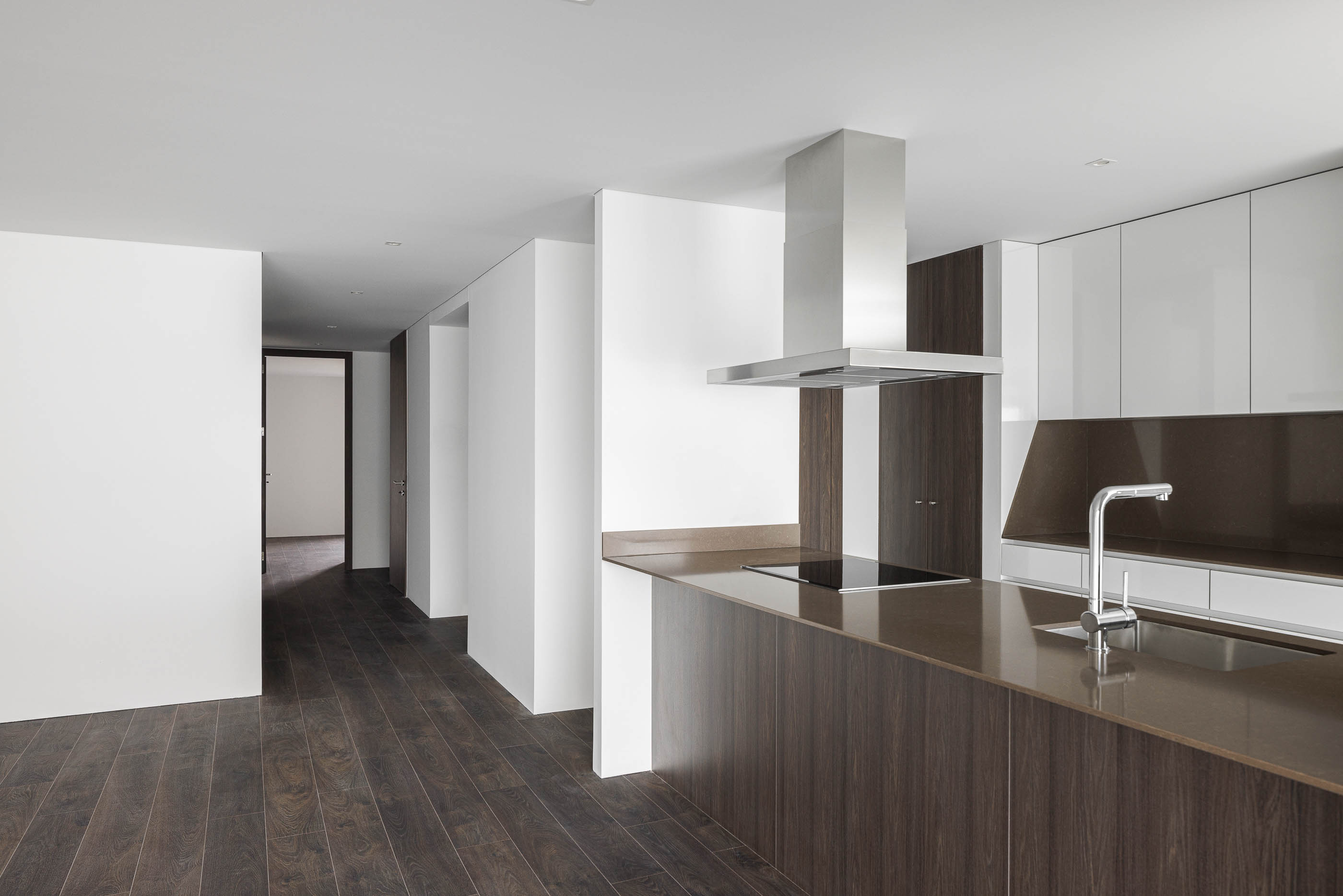 Cozinha: Ilha central com bancada em pedra escura e armários brancos e em madeira. — Evolution Apartments Housing arquitetura António Paulo Marques, Arquiteto e Associados em Matosinhos