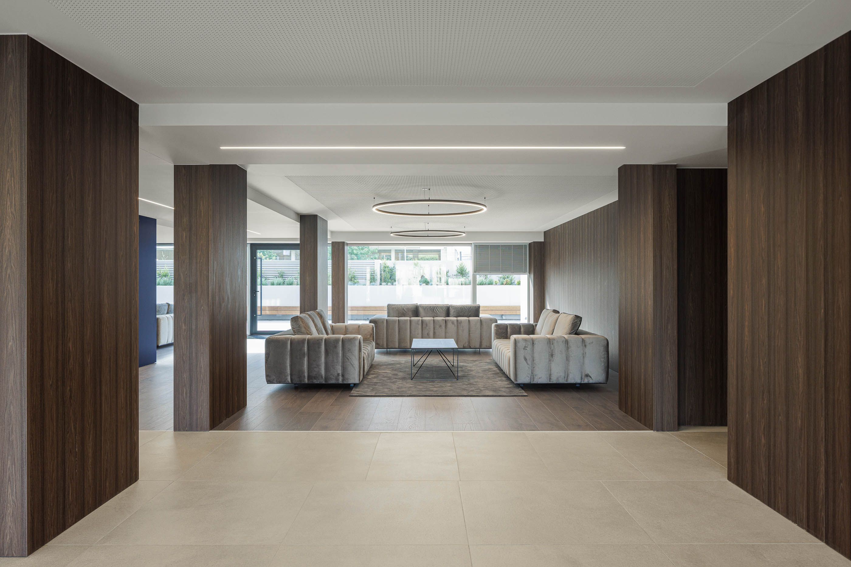 Lobby: Espaço amplo com sofás em tons neutros, pavimento em madeira e iluminação circular. — Evolution Apartments Housing arquitetura António Paulo Marques, Arquiteto e Associados em Matosinhos