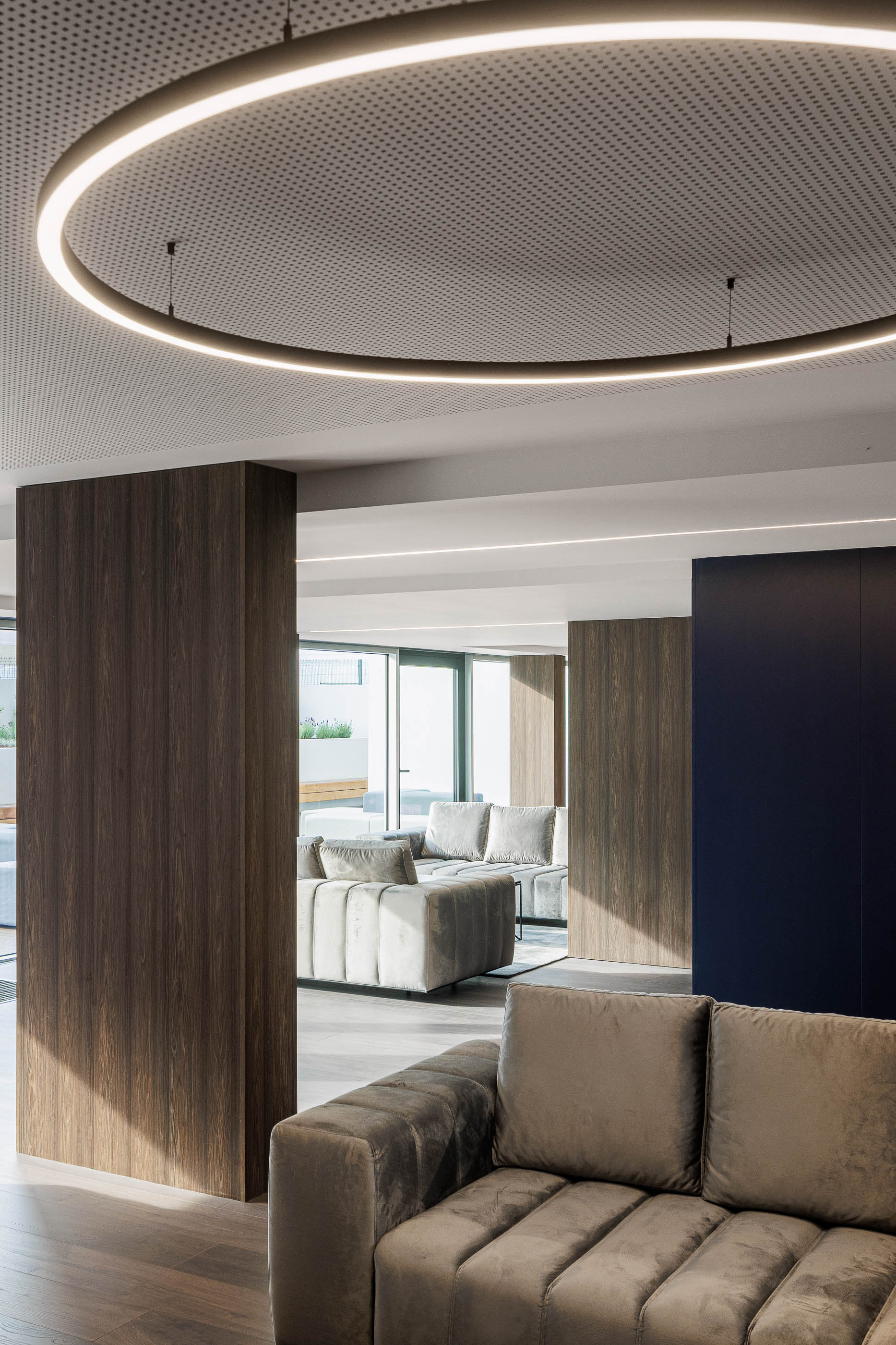 Lobby: Sofá em veludo cinzento, parede revestida a madeira e candeeiro circular suspenso. — Evolution Apartments Housing arquitetura António Paulo Marques, Arquiteto e Associados em Matosinhos