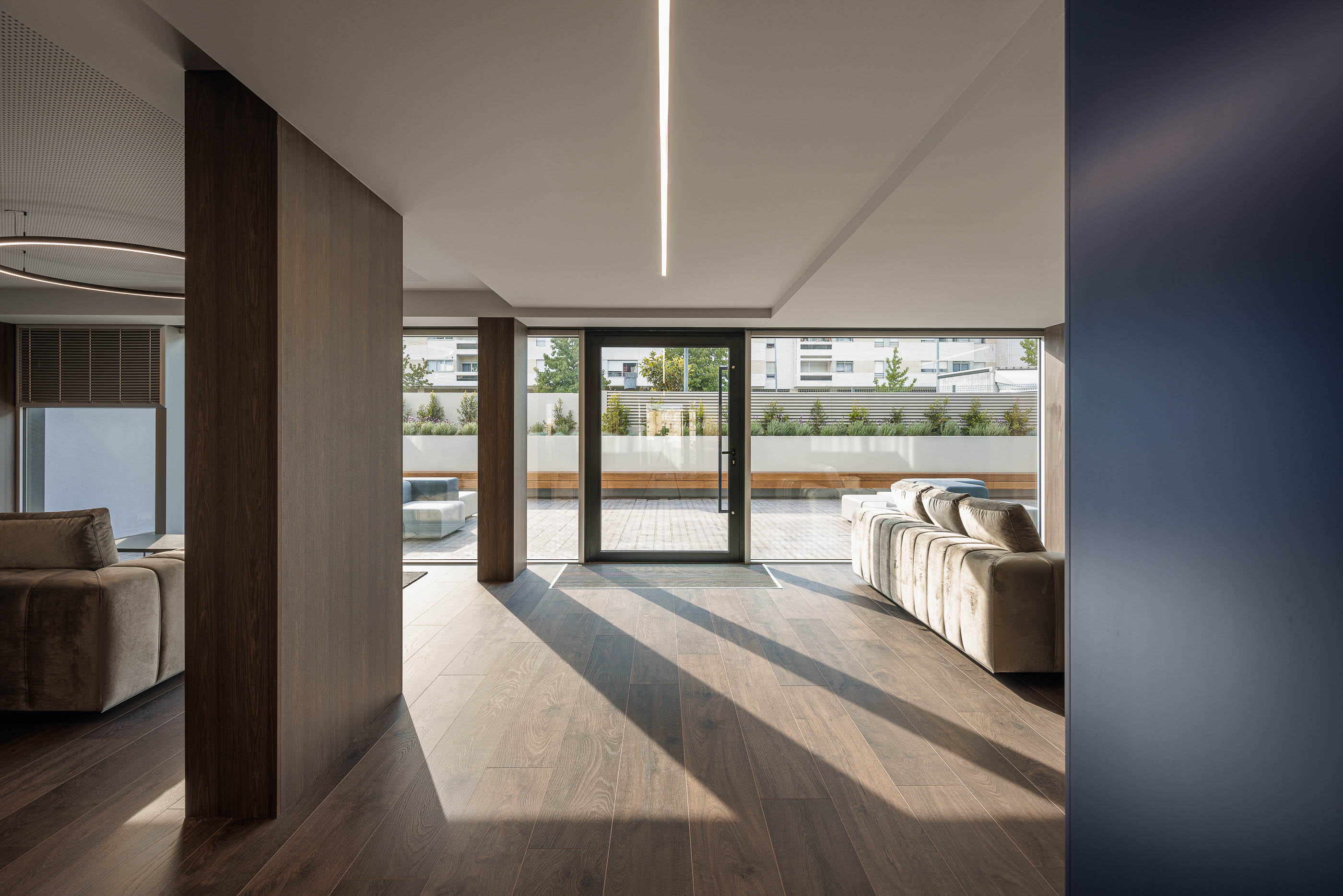 Lobby: Sofás em veludo cinzento, pavimento em madeira e acesso ao terraço exterior. — Evolution Apartments Housing arquitetura António Paulo Marques, Arquiteto e Associados em Matosinhos