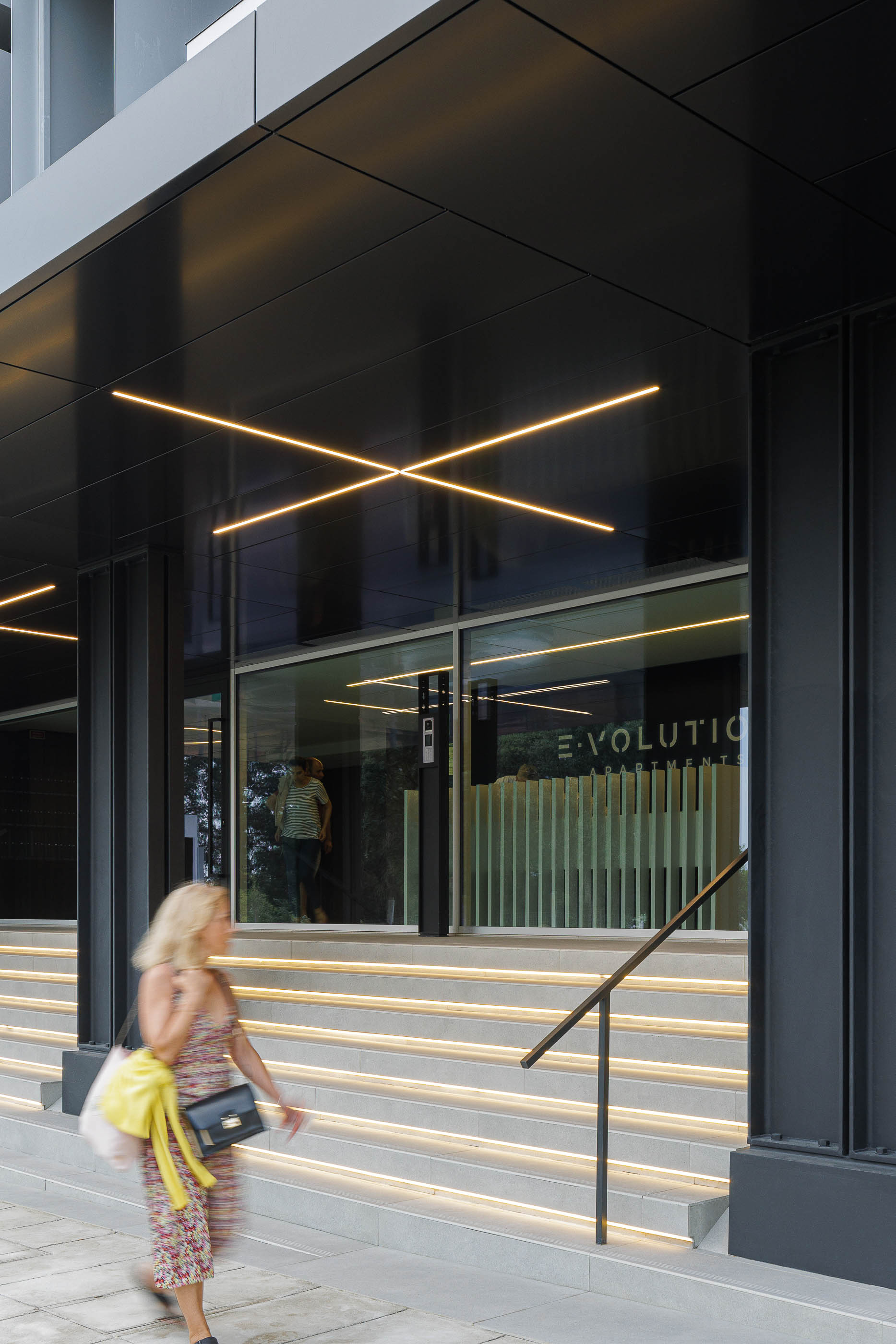 Entrada: Escadaria iluminada com candeeiros lineares e revestimento em painéis pretos. — Evolution Apartments Housing arquitetura António Paulo Marques, Arquiteto e Associados em Matosinhos