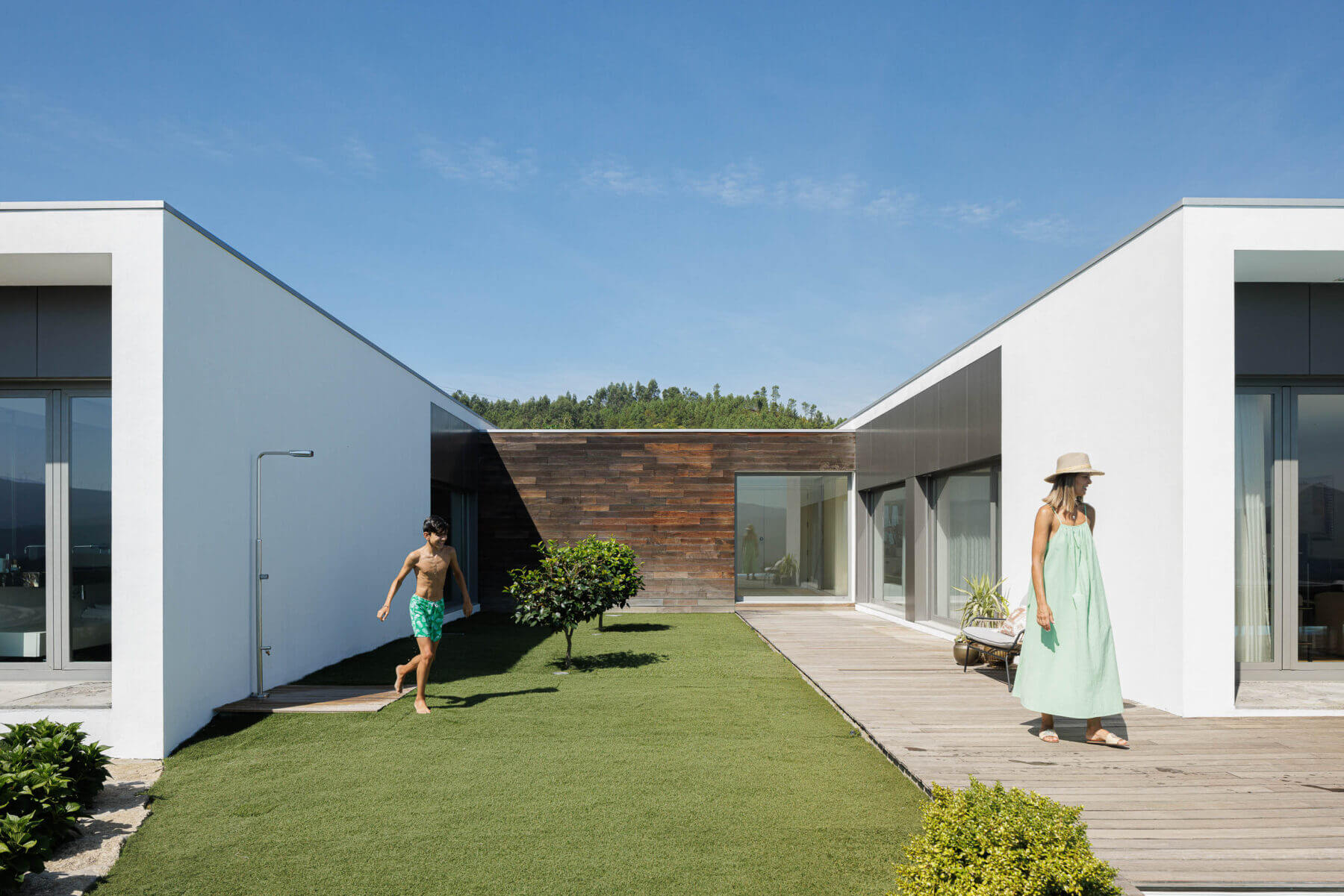 Exterior: Vista do pátio interior com relvado, deck de madeira, fachada em madeira e volumes brancos da casa. — Casa do Alto arquitetura Jorge Martins arquiteto em Celorico de Basto