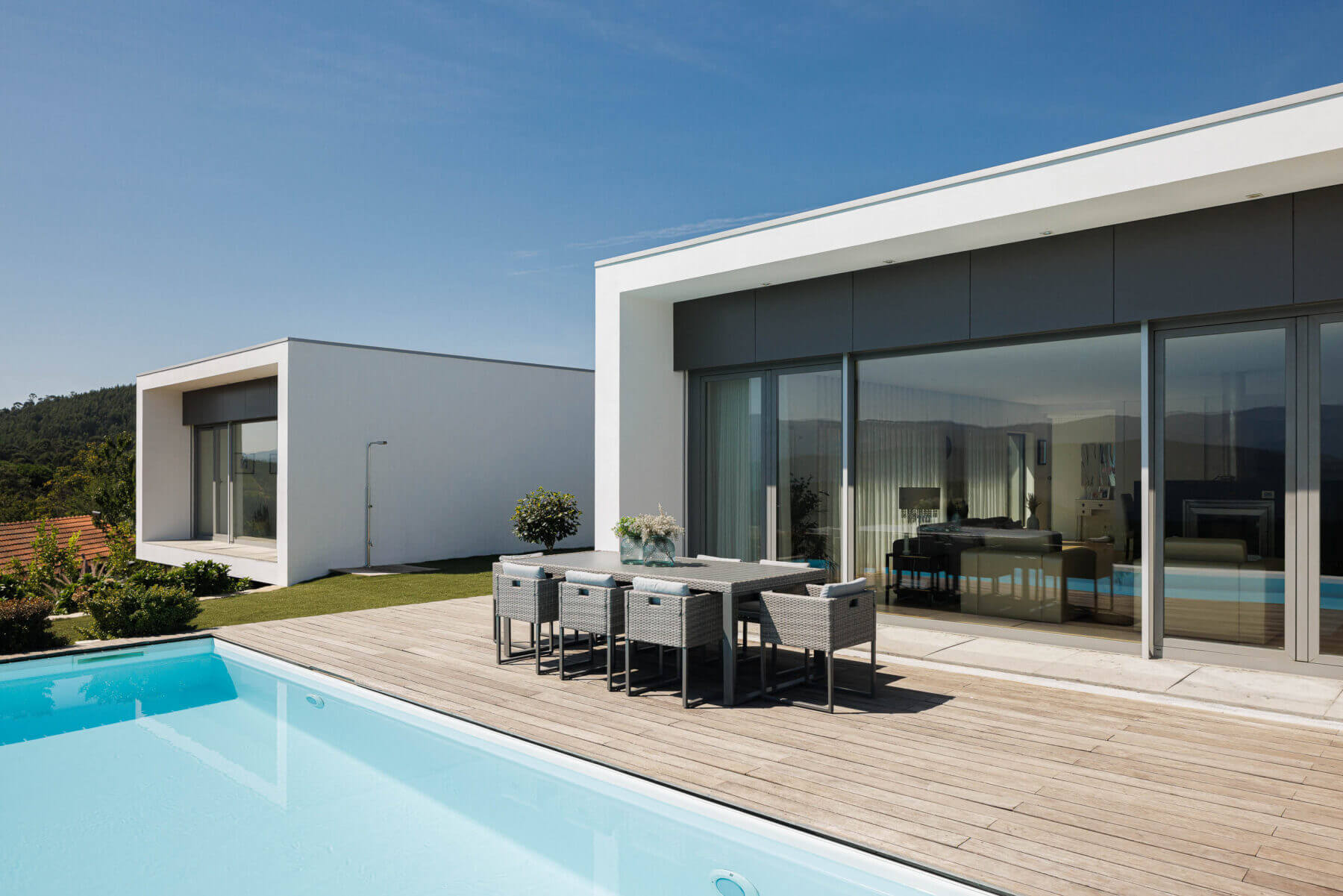 Exterior: Piscina com deck de madeira, mesa de refeições e vista panorâmica. Fachada branca da casa com grandes janelas. — Casa do Alto arquitetura Jorge Martins arquiteto em Celorico de Basto